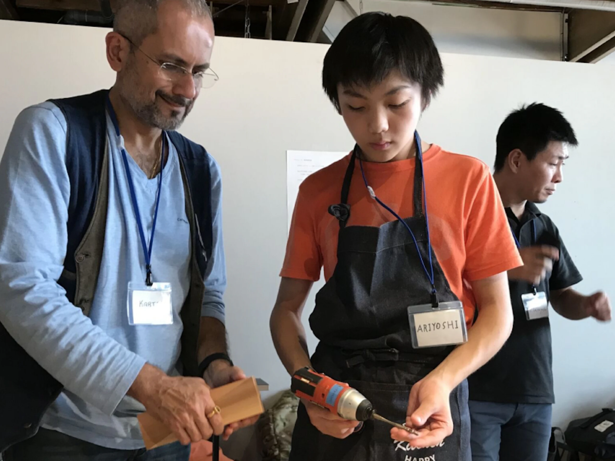 Two people at the Kidsdoor Tokyo design camp hosted by MillerKnoll. One holds a power drill while the other holds a block of wood.