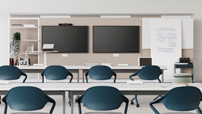 Aula moderna con dos pantallas grandes, una pizarra blanca con notas y una mesa blanca larga rodeada de sillas color verde azulado. Estantería con libros y plantas al fondo.