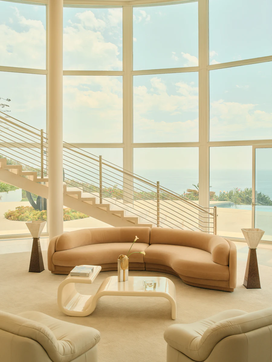 Sunlit modern living room with large curved beige sofa and glass coffee table