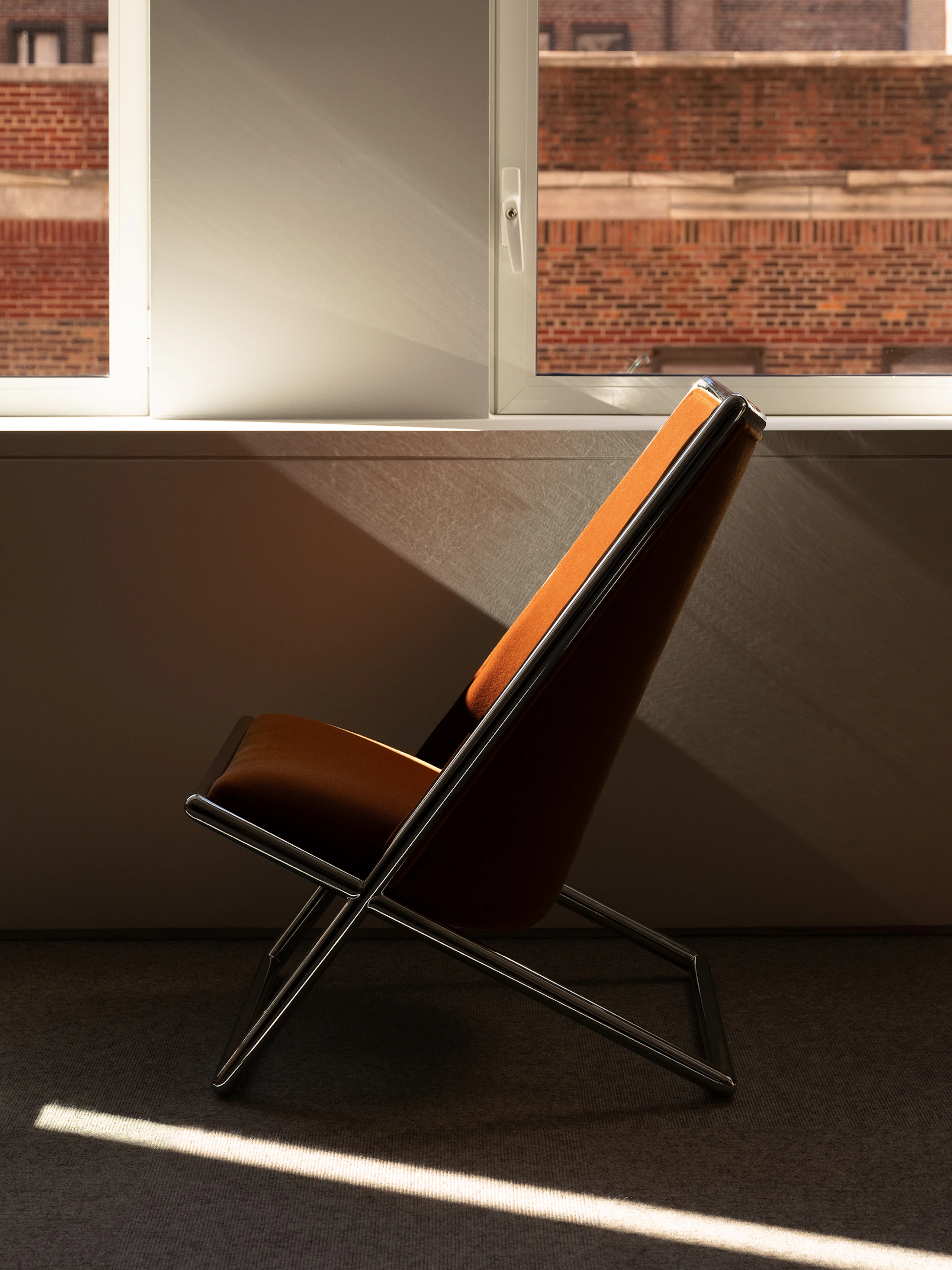 Scissor Chair designed by Ward Bennett upholstered with Mohair Supreme in Cognac with a chrome frame, viewed in profile in a showroom setting.