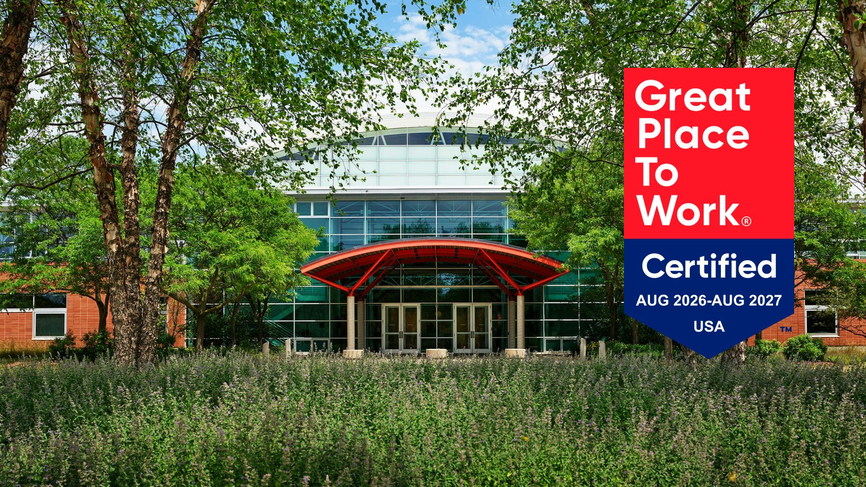 An exterior front view of the MillerKnoll Greenhouse manufacturing facility with the red and blue Great Place to Work certified 2026-2027 badge overlayed on top.