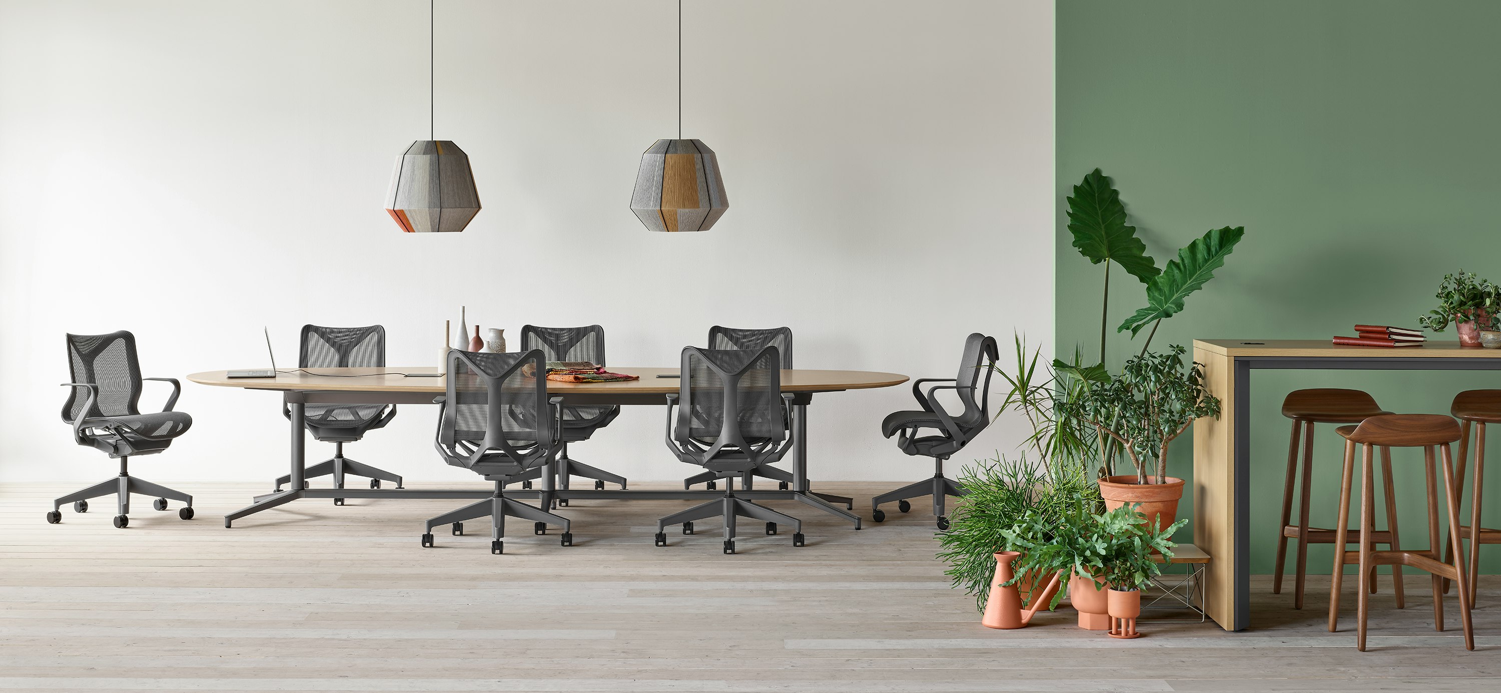 A Y base Headway conference table surrounded by seven Cosm chairs in an open conference space with a Headway communal table with Crosshatch stools nearby.