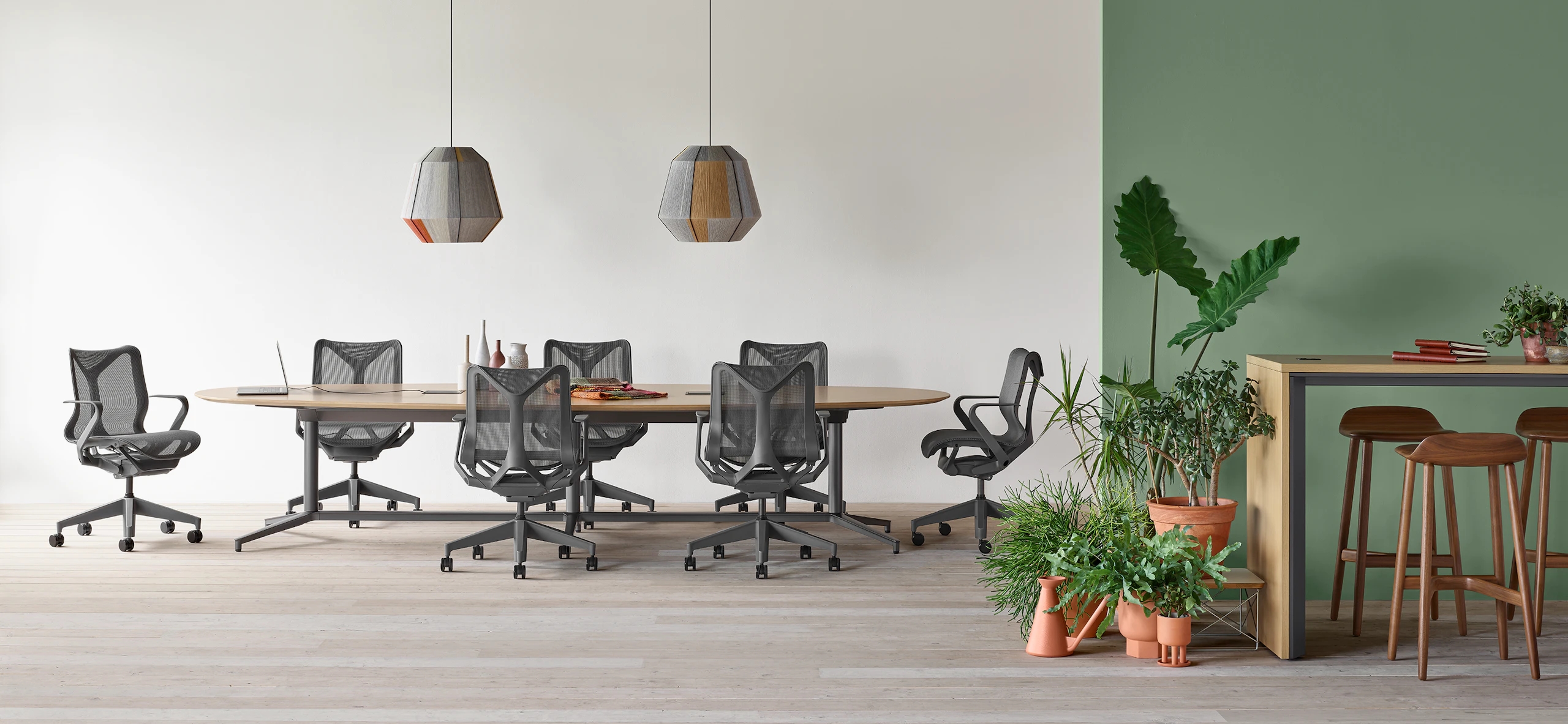 A Y base Headway conference table surrounded by seven Cosm chairs in an open conference space with a Headway communal table with Crosshatch stools nearby.