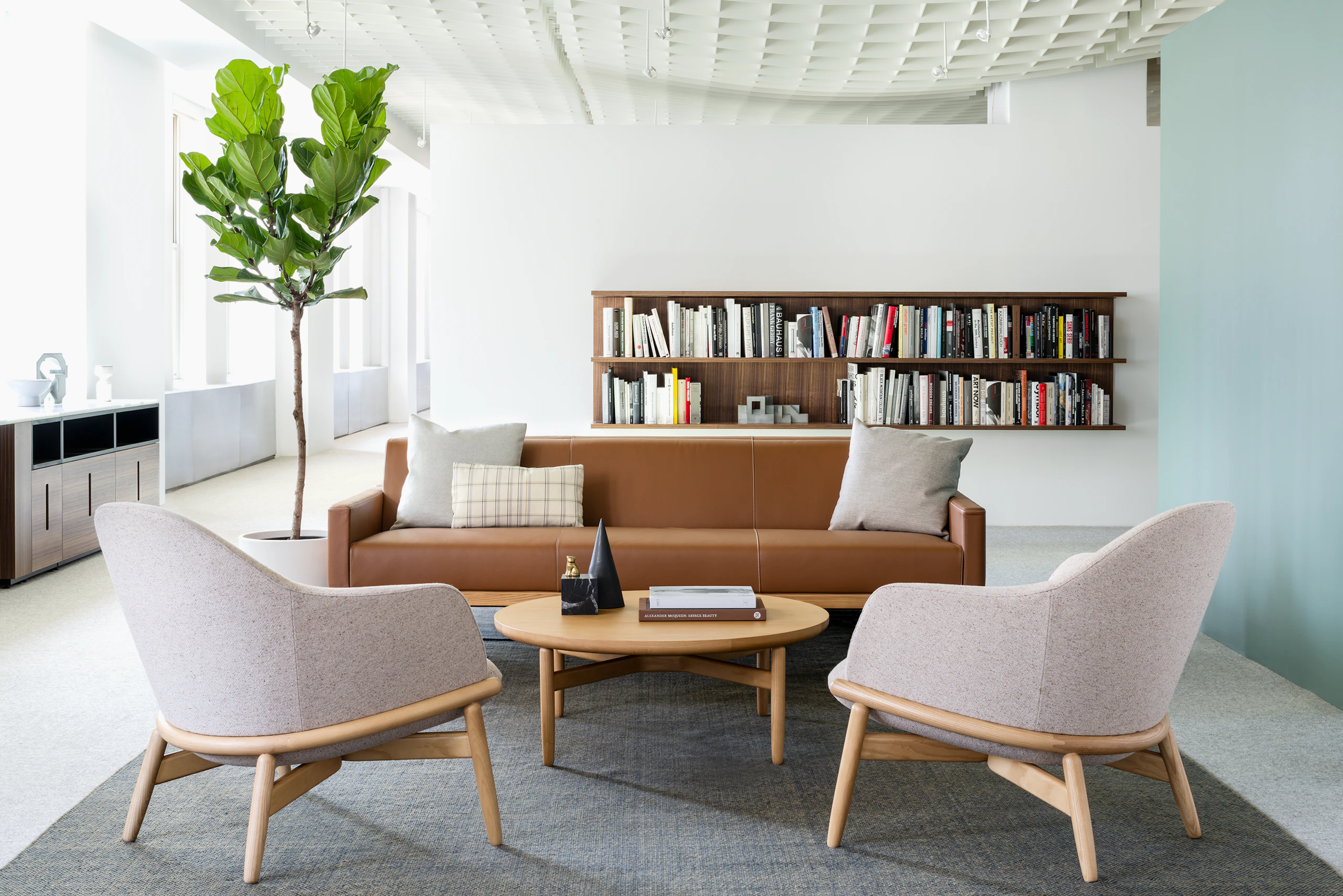 A lounge area featuring a brown Wood Base sofa, two light gray Reframe mid-back lounge chairs, and a round Reframe occasional table.