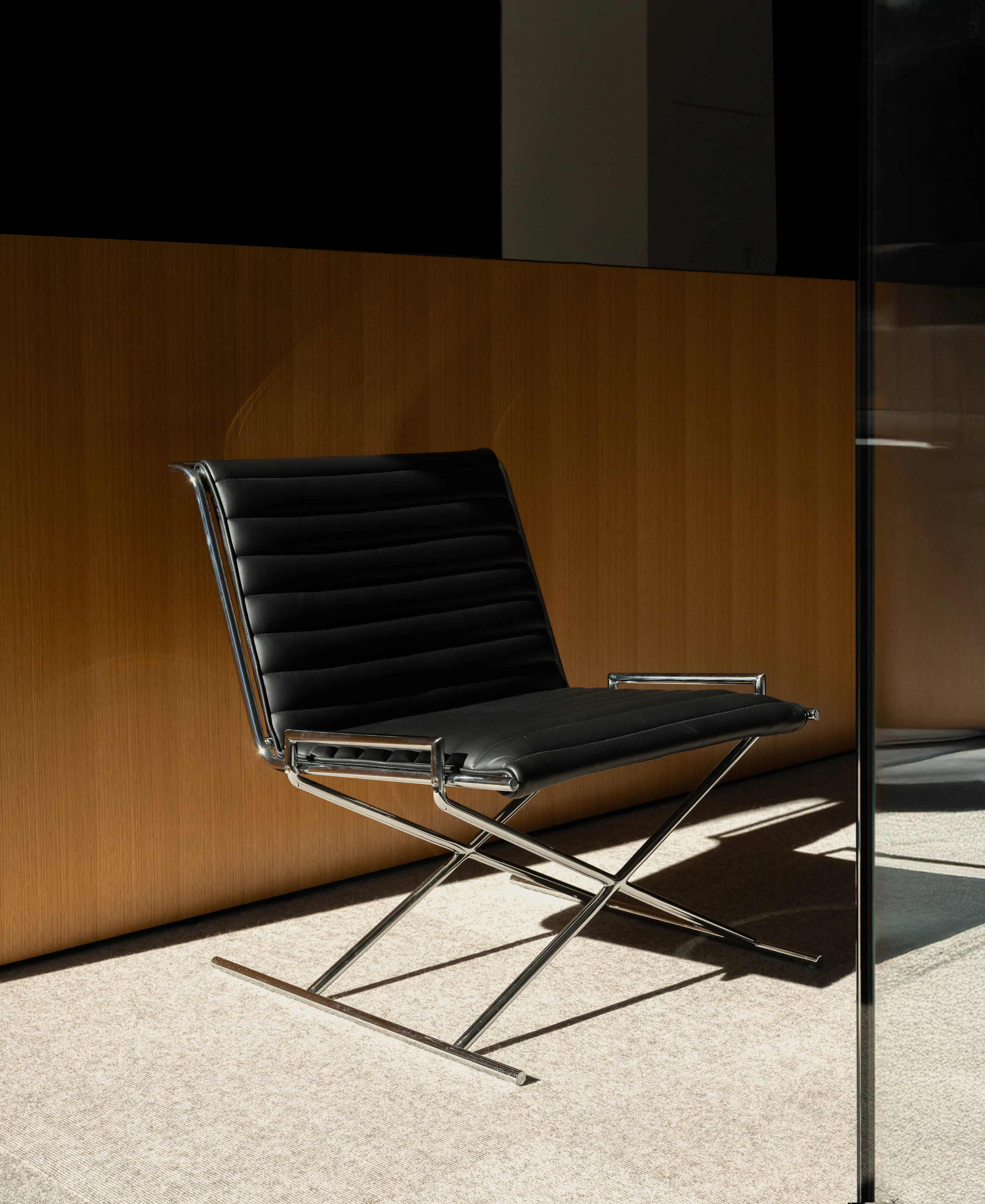 Sled Chair designed by Ward Bennett upholstered with black leather with a chrome frame, viewed in an office setting at an angle.