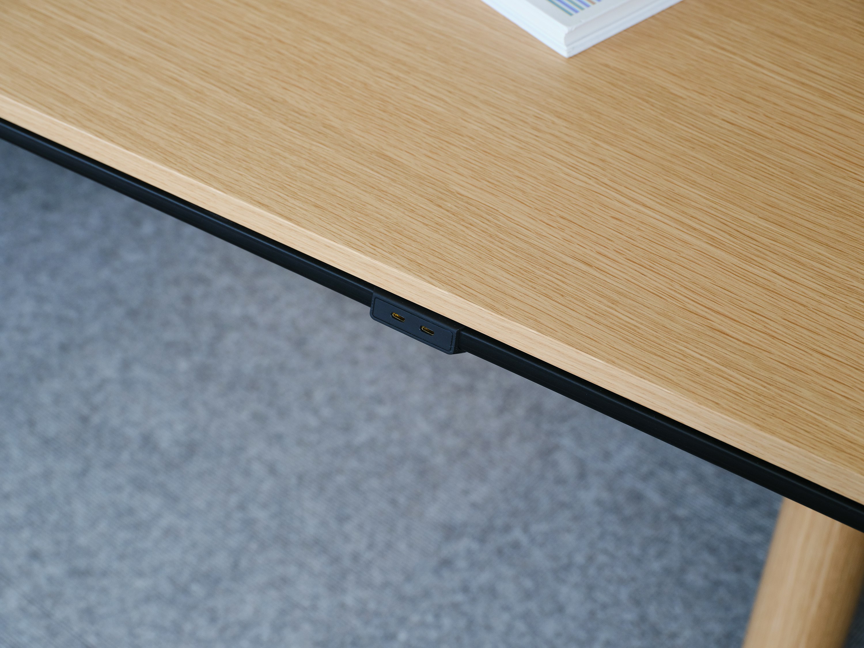 Detail view of the Ascent Conference Table edge power in black with a Natural Rift Cut Oak tabletop, viewed at an angle.