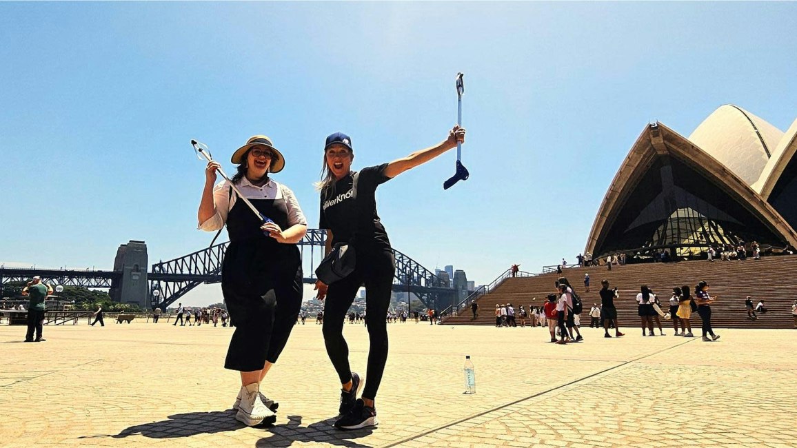 Two MillerKnoll associates holding rubbish-grabbing devices while posing outside of the Sydney Opera House.