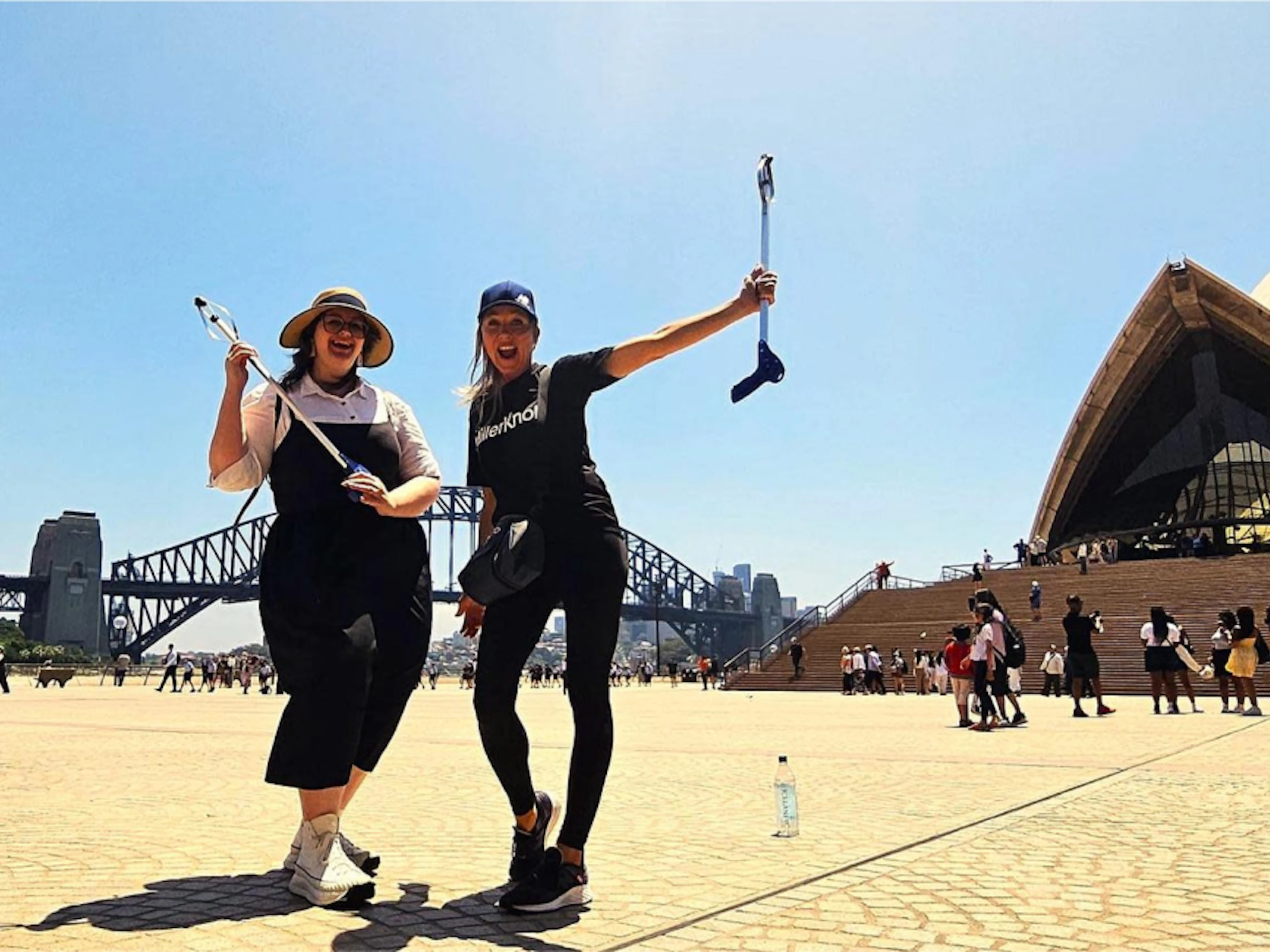 Two MillerKnoll associates holding rubbish-grabbing devices while posing outside of the Sydney Opera House.