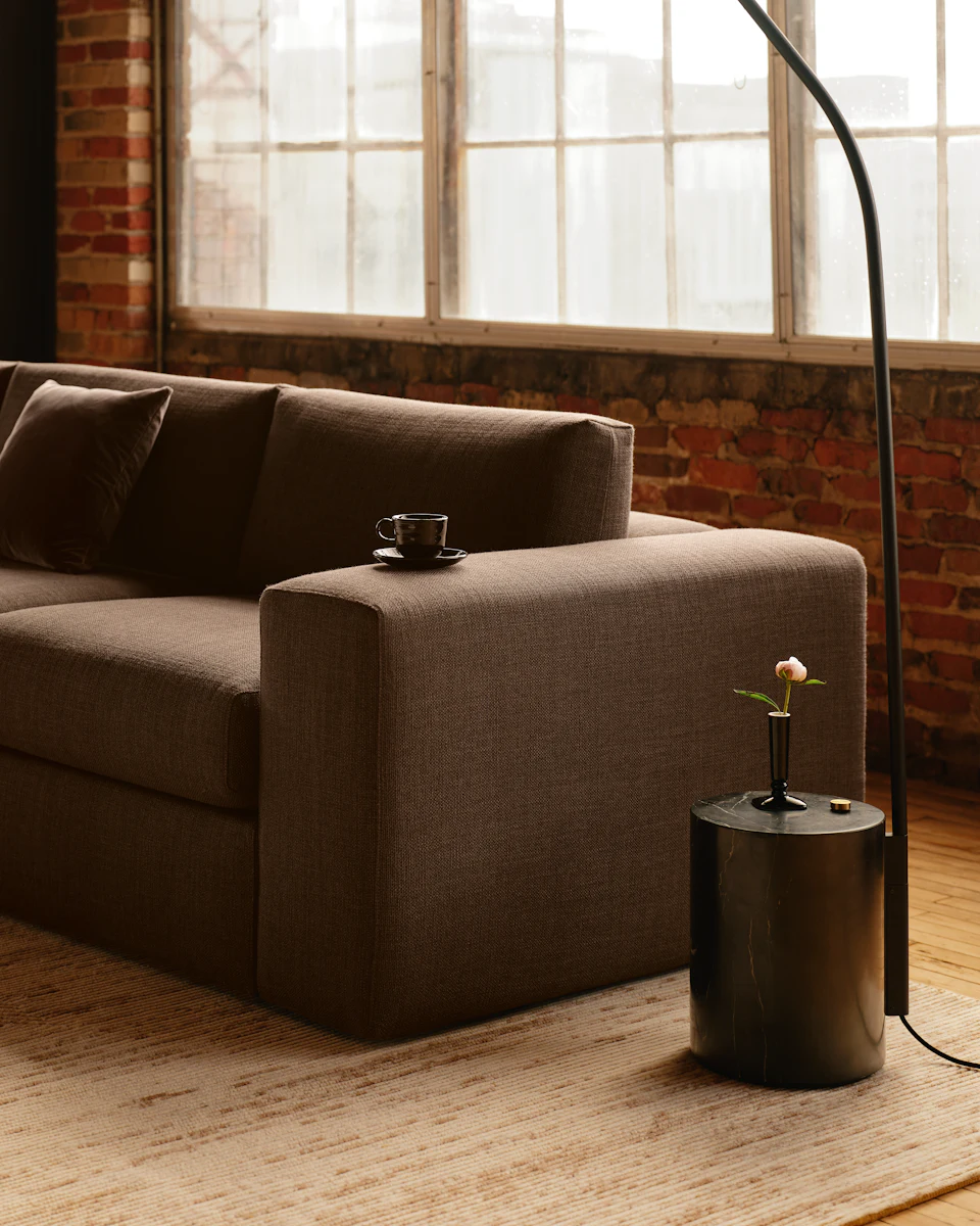 A gray sectional sofa in a bright loft with a small side table and a cup on the armrest.