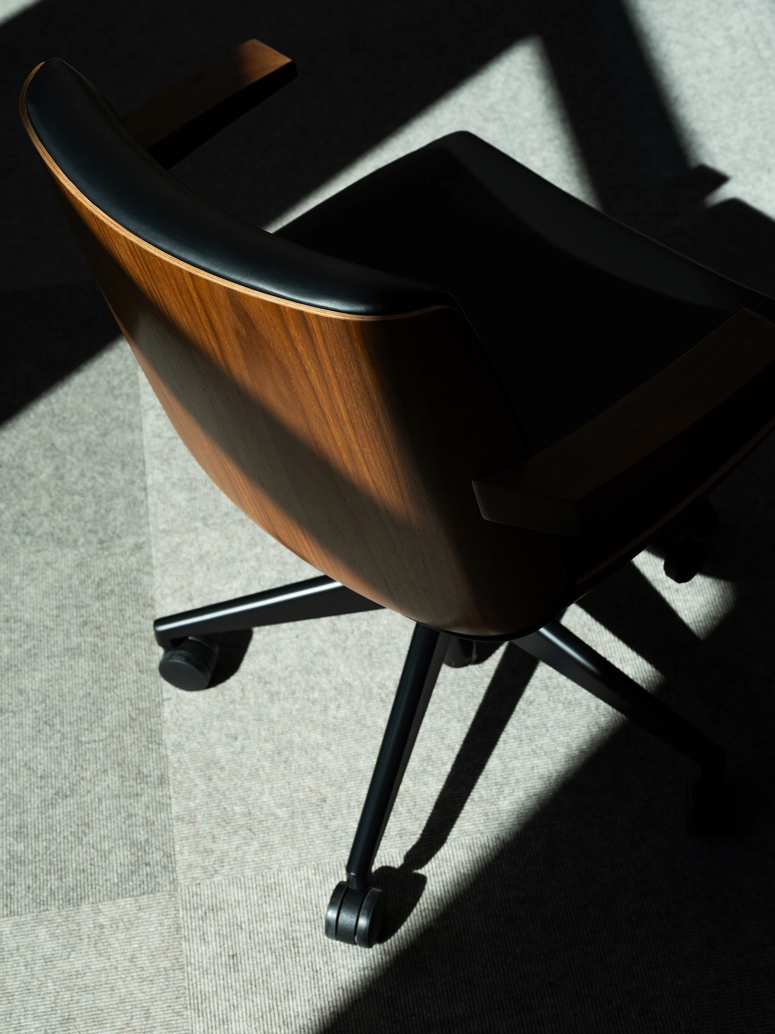 Detail view of a low back Clamshell Conference Chair in Walnut upholstered with black leather, viewed from above.