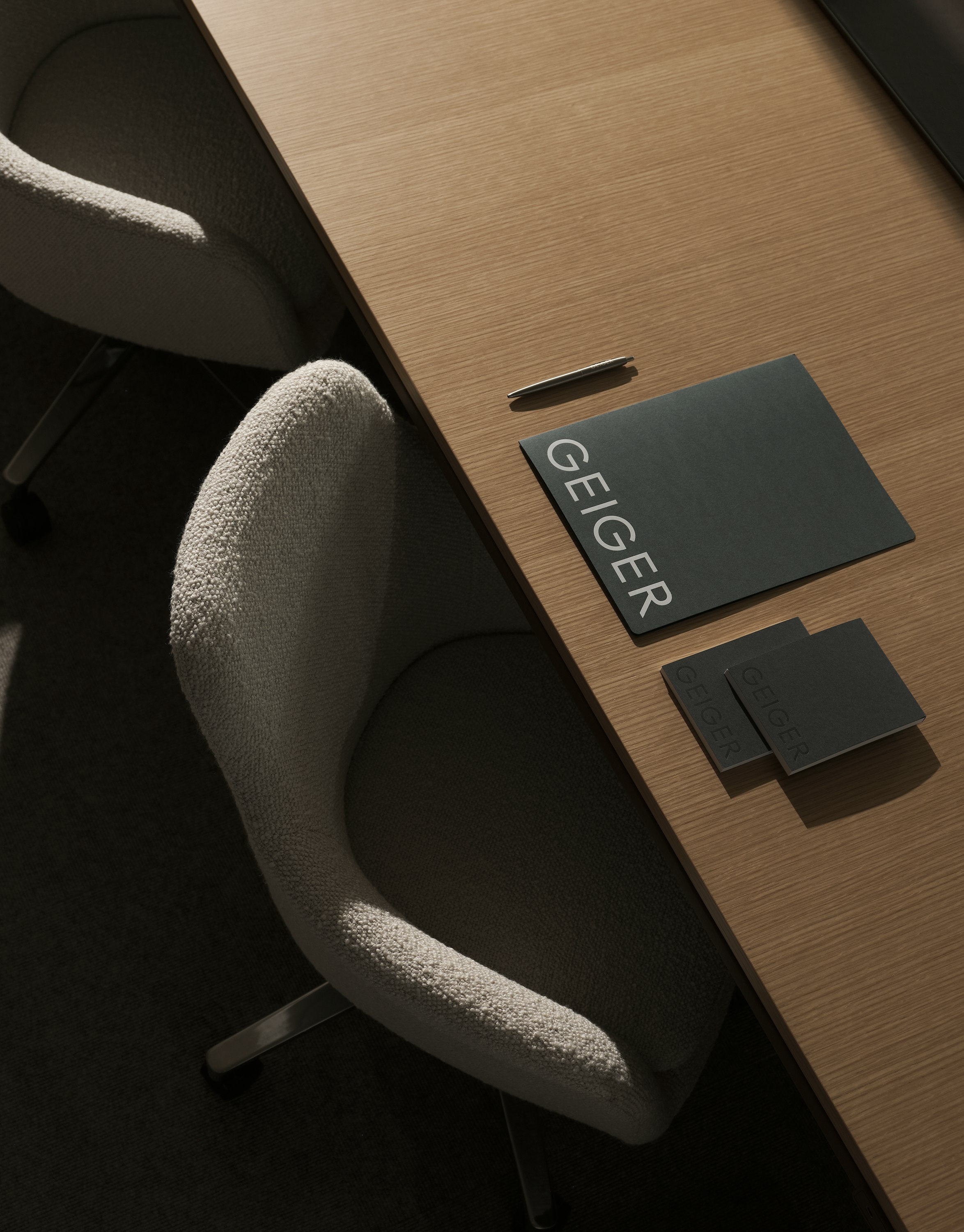 Ascent Conference Table in Natural Rift Cut Oak styled with various Geiger amenities, with two Saiba Chairs upholstered with Pristina in Dove, viewed from above at an angle.