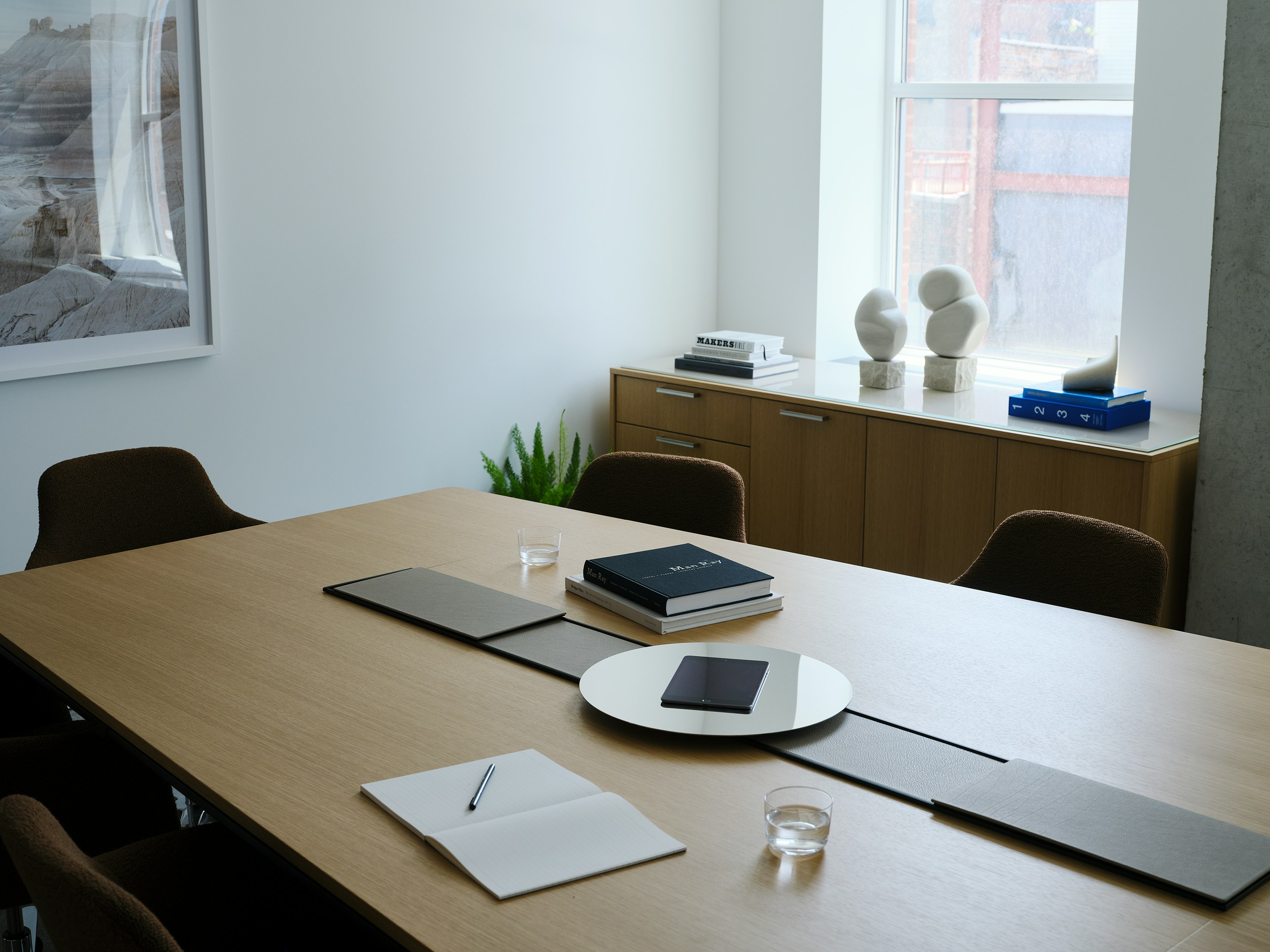 Ascent Conference Table designed by EOOS in Natural Rift Cut Oak with a leather-covered power trough and  chrome accessory tray, with Saiba Chairs and a JD Credenza, viewed at an angle in a conference room setting.