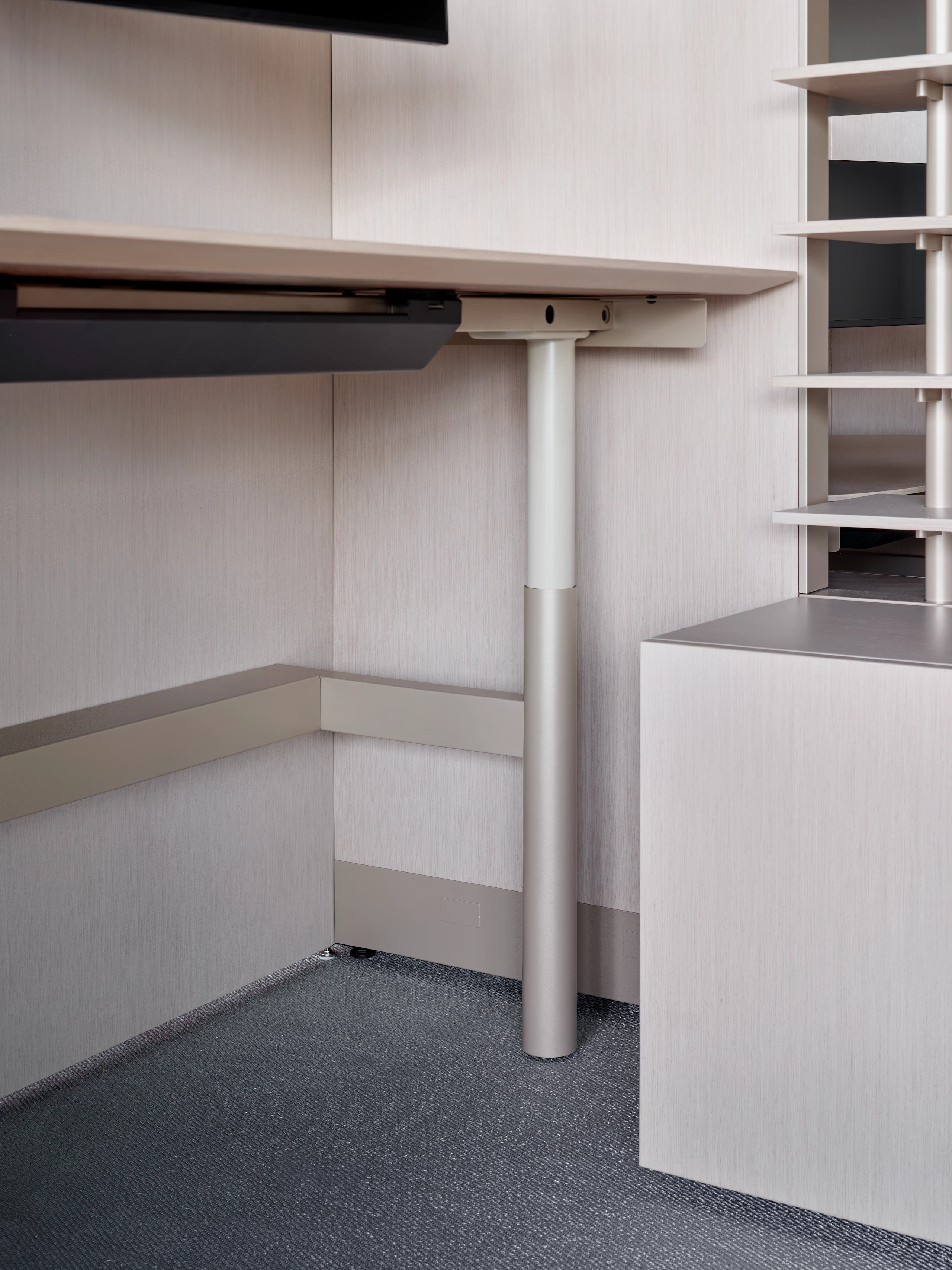 A height adjustable desk is viewed from an angle with open shelving and system panels.