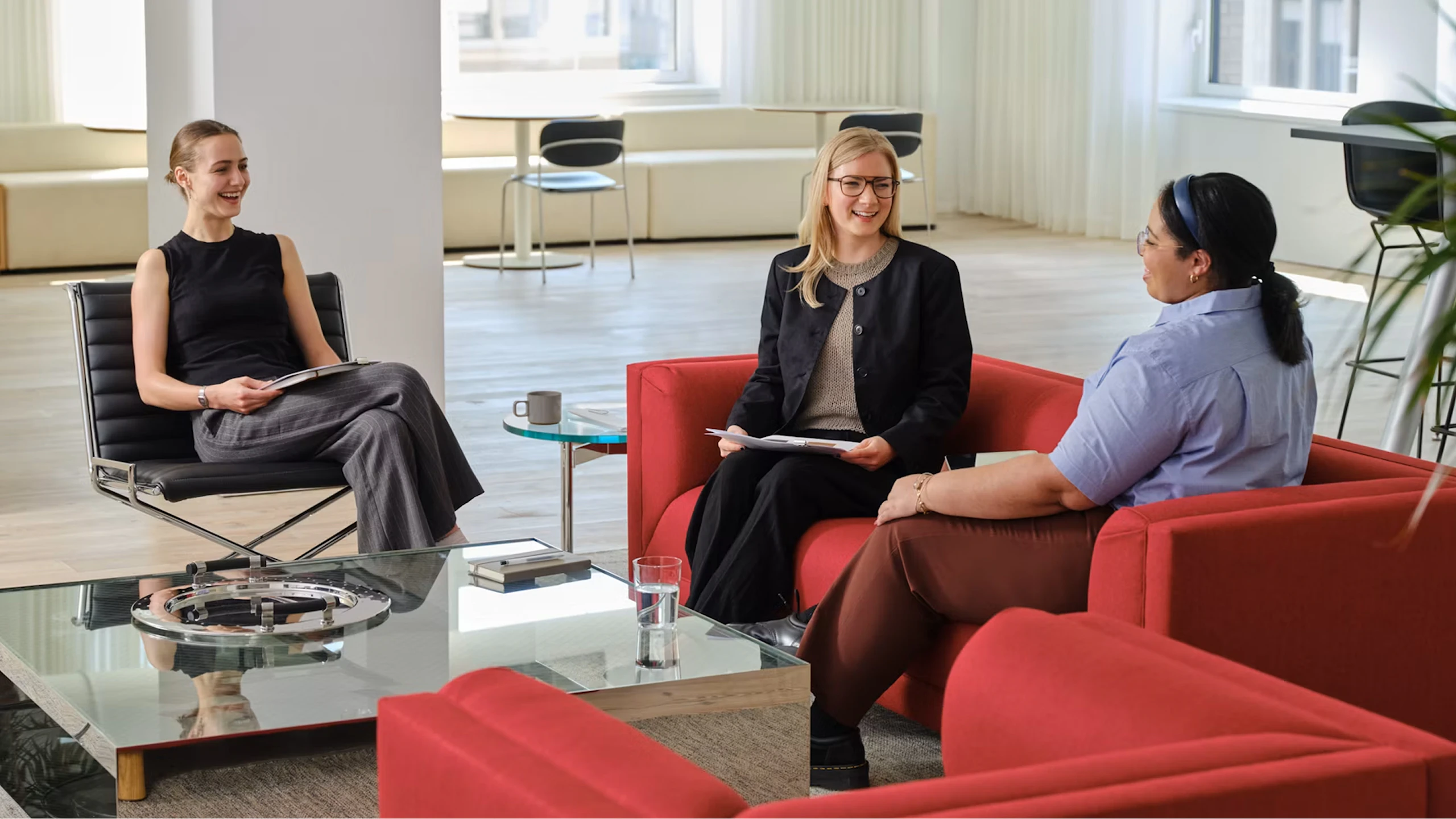 Three women seated on a red sofa and black side chair around a reflective D'Urso Coffee Table from Knoll.