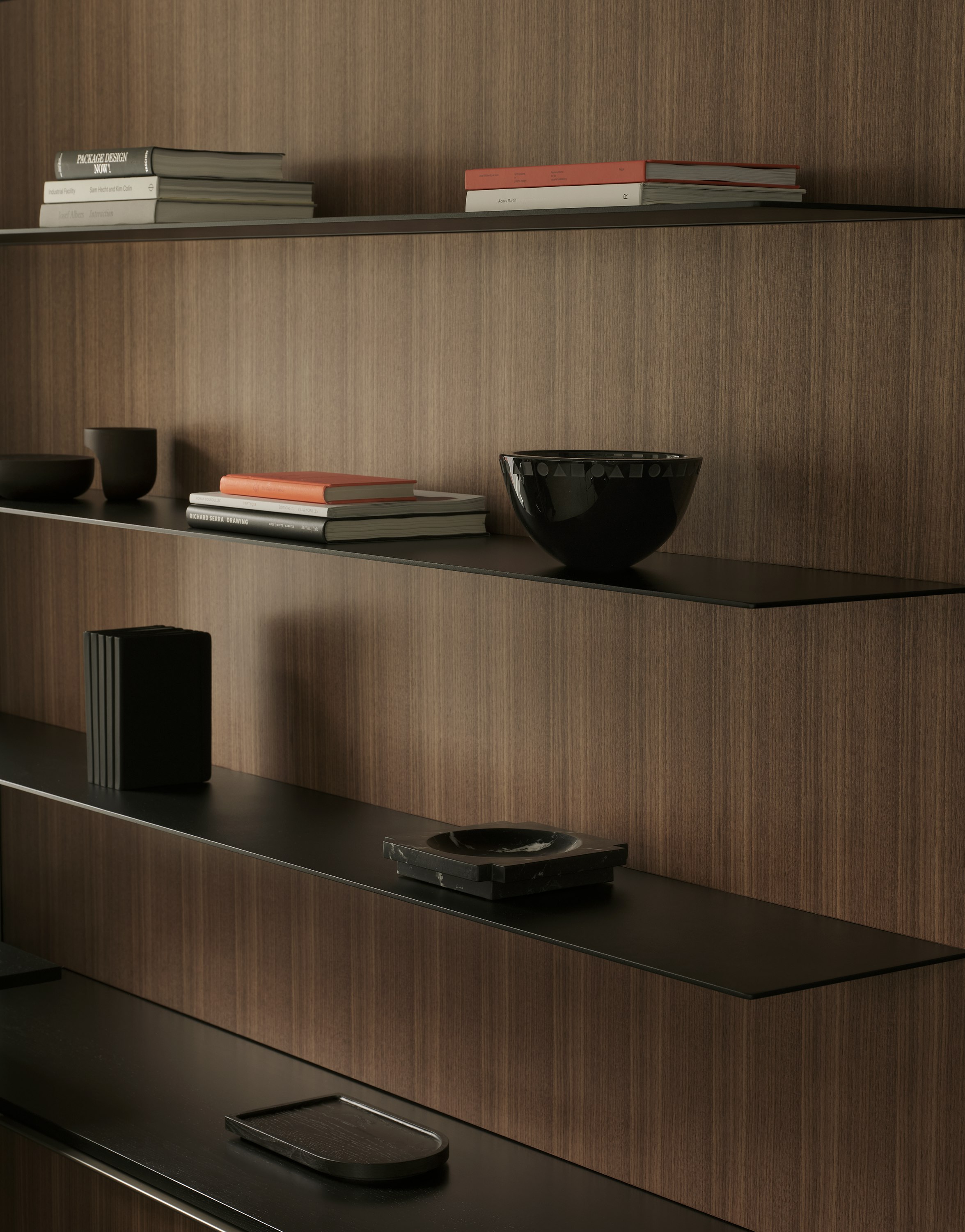 Detail view of a Geiger One Private Office storage wall in Natural Quarter Cut Walnut with matte black metal shelves, styled with books and other items, viewed at an angle.