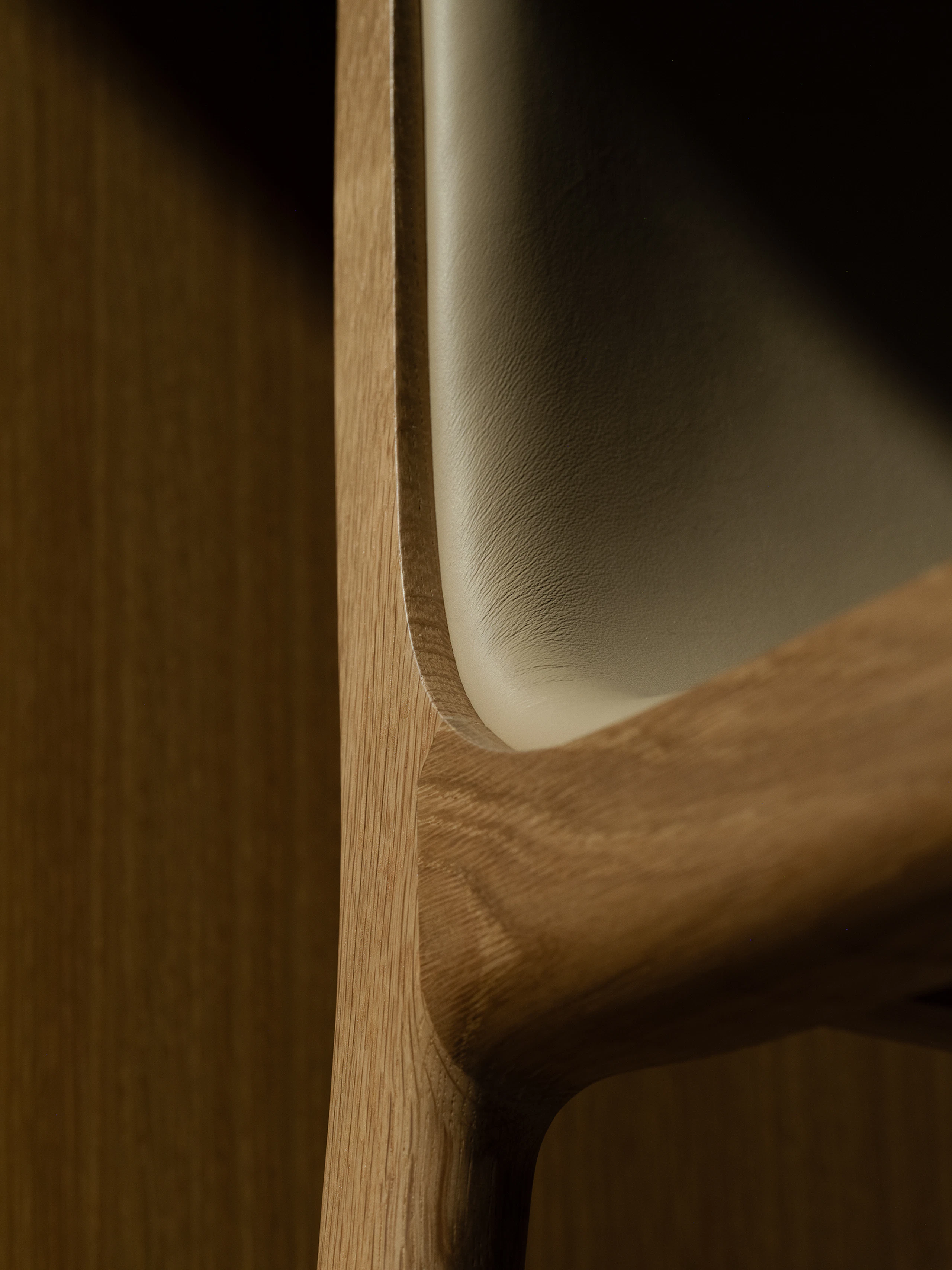 Detail view of a Lijn Stool frame and backrest in Natural Oak fully upholstered with Bristol leather in Champagne, viewed from below at an angle.