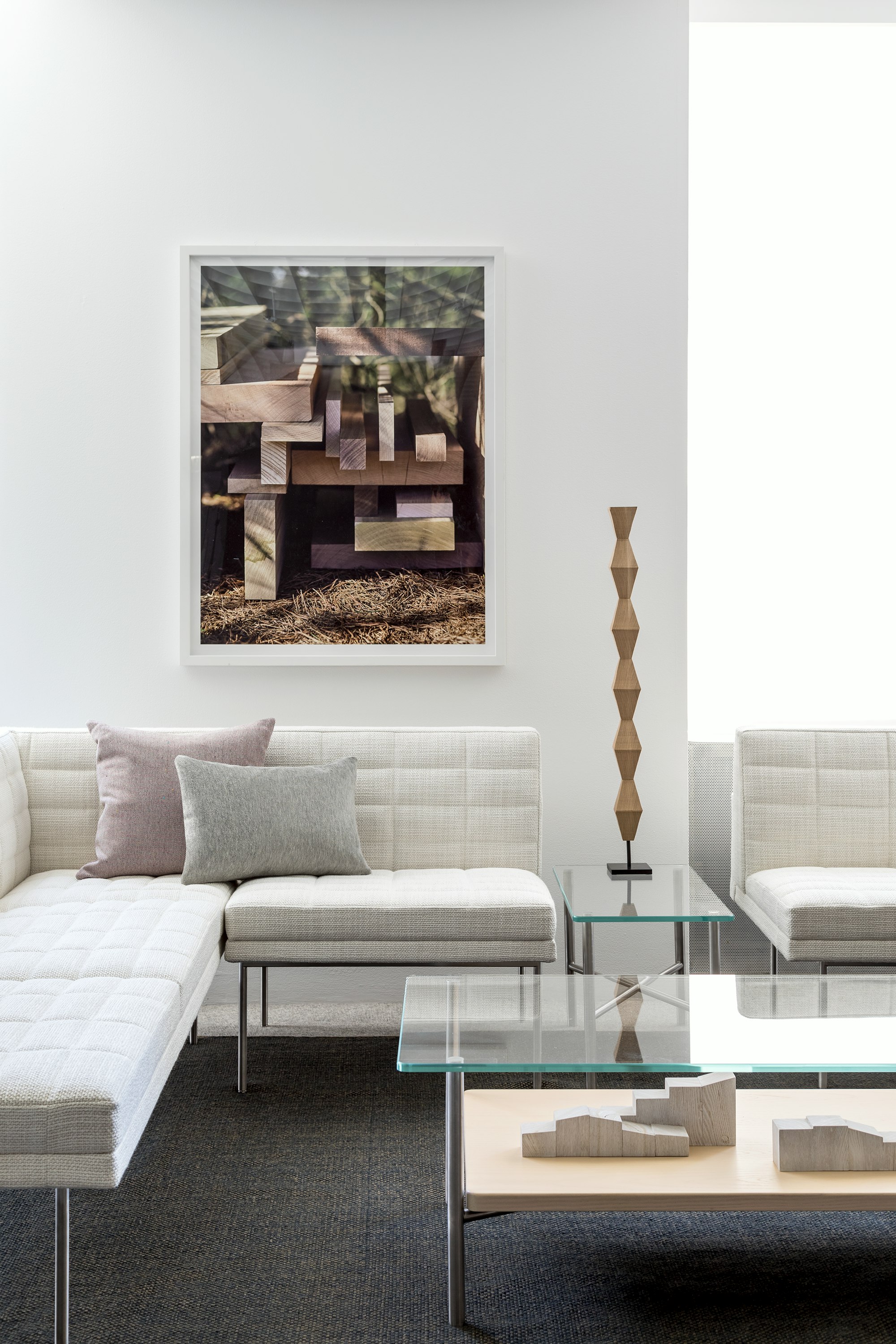 A lounge featuring a rectangular Layer coffee table with a glass top and wood shelf, complemented by off-white Tuxedo Component Lounge Seating.