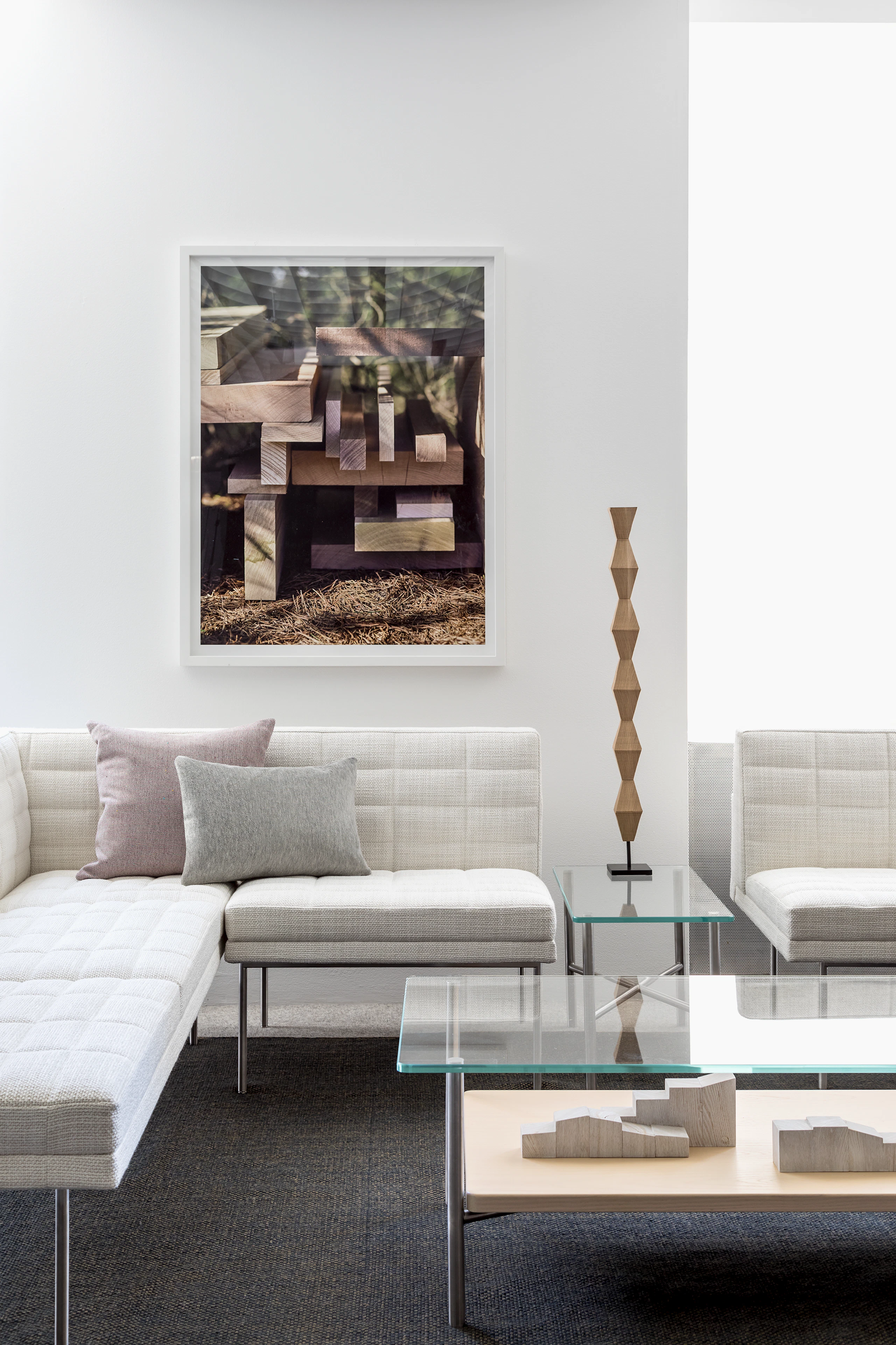 A lounge featuring a rectangular Layer coffee table with a glass top and wood shelf, complemented by off-white Tuxedo Component Lounge Seating.
