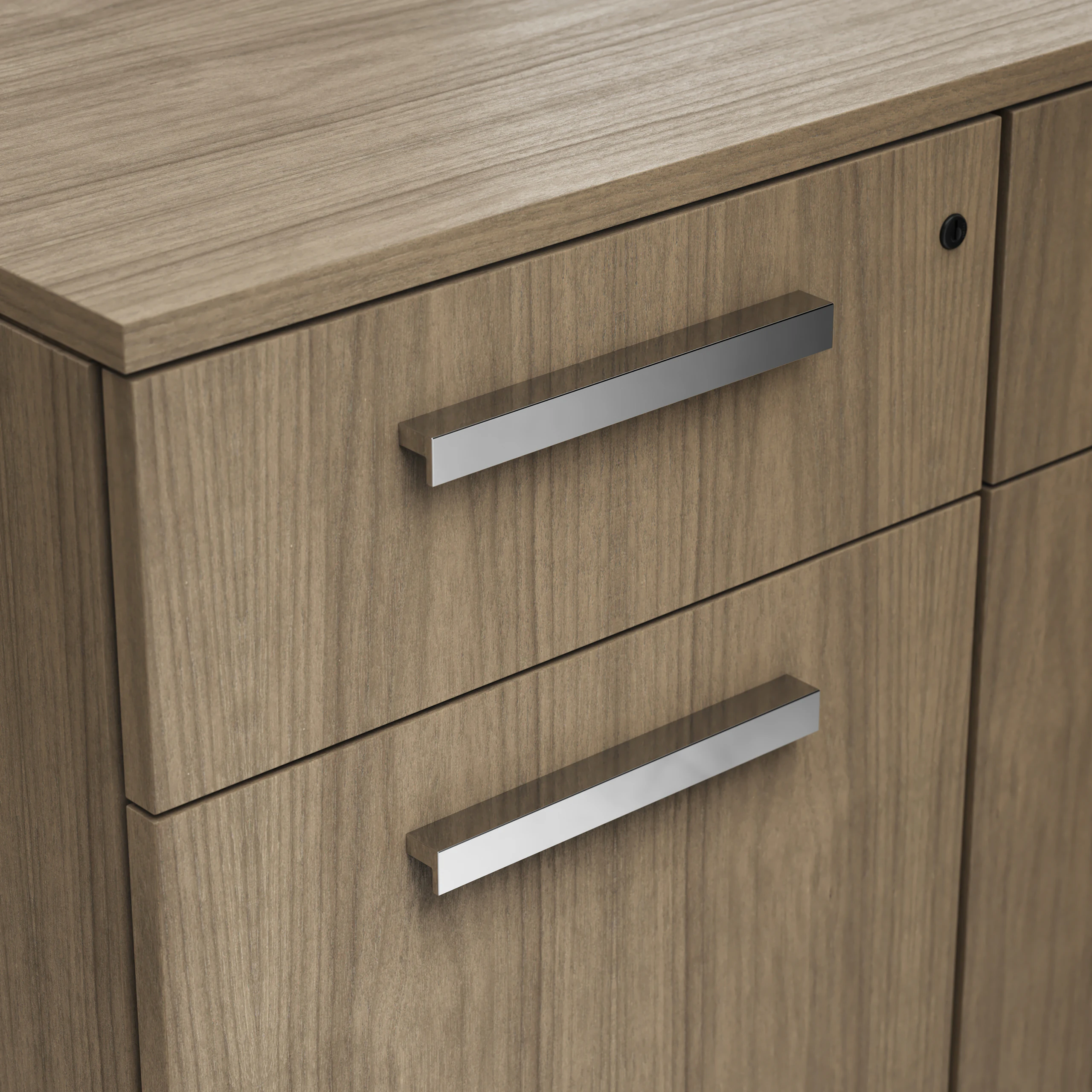 Detail shot of the Geiger One Casegoods ledge pull option in Chrome on a Natural Flat Cut Walnut drawer front viewed from an angle.
