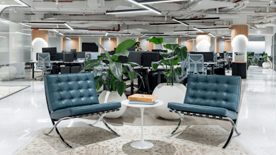 An open plan office with a pair of Barcelona Chairs in the foreground and desking in the background.