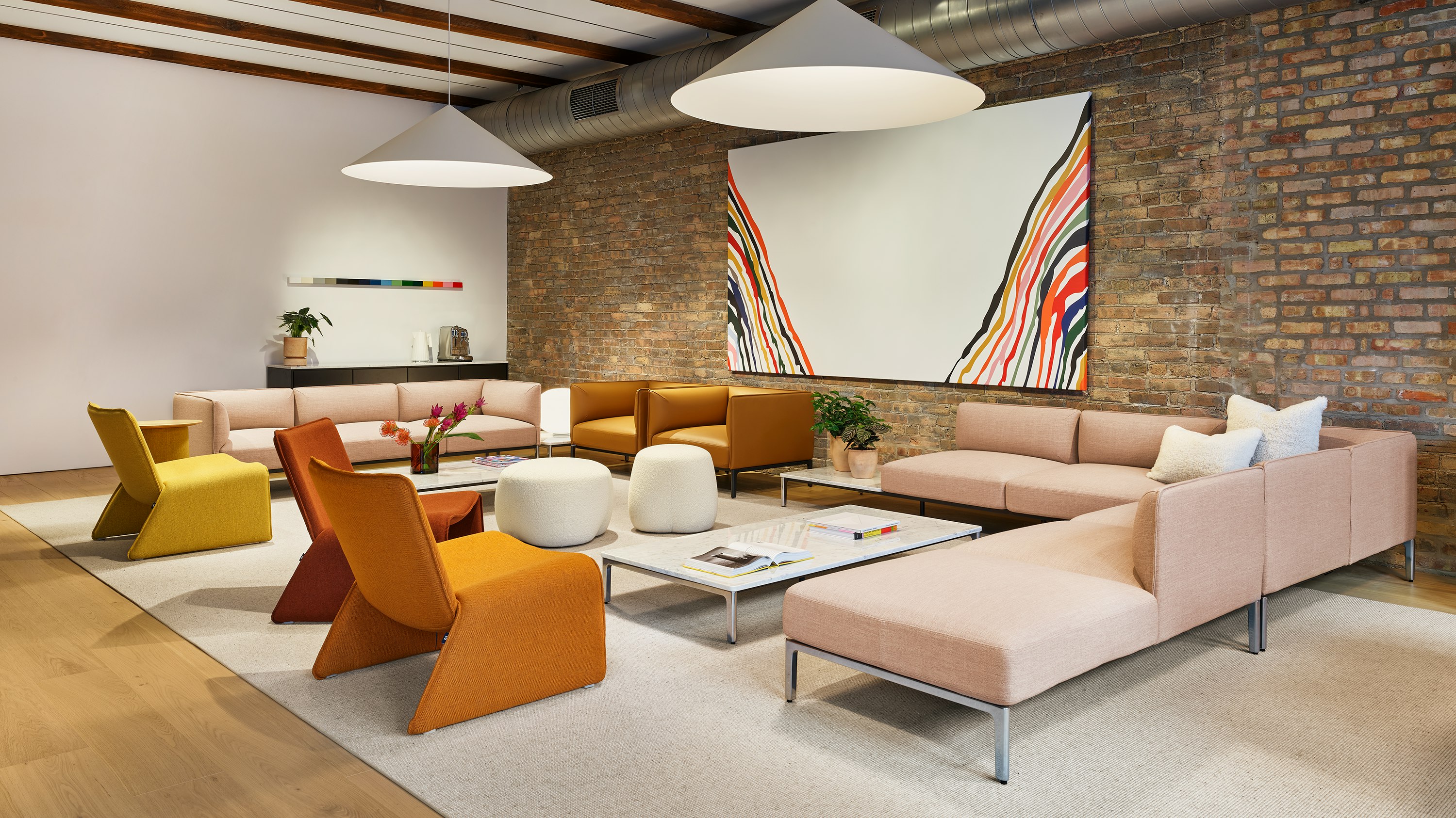 A lounge area at NaughtOne's Fulton Market showroom including an arrangement of pink upholstered Mimo modular seating, leather Mimo Club Chairs, marble top Mimo Coffee Tables, Truffle pouf and Fin Lounge chairs in orange and yellow.