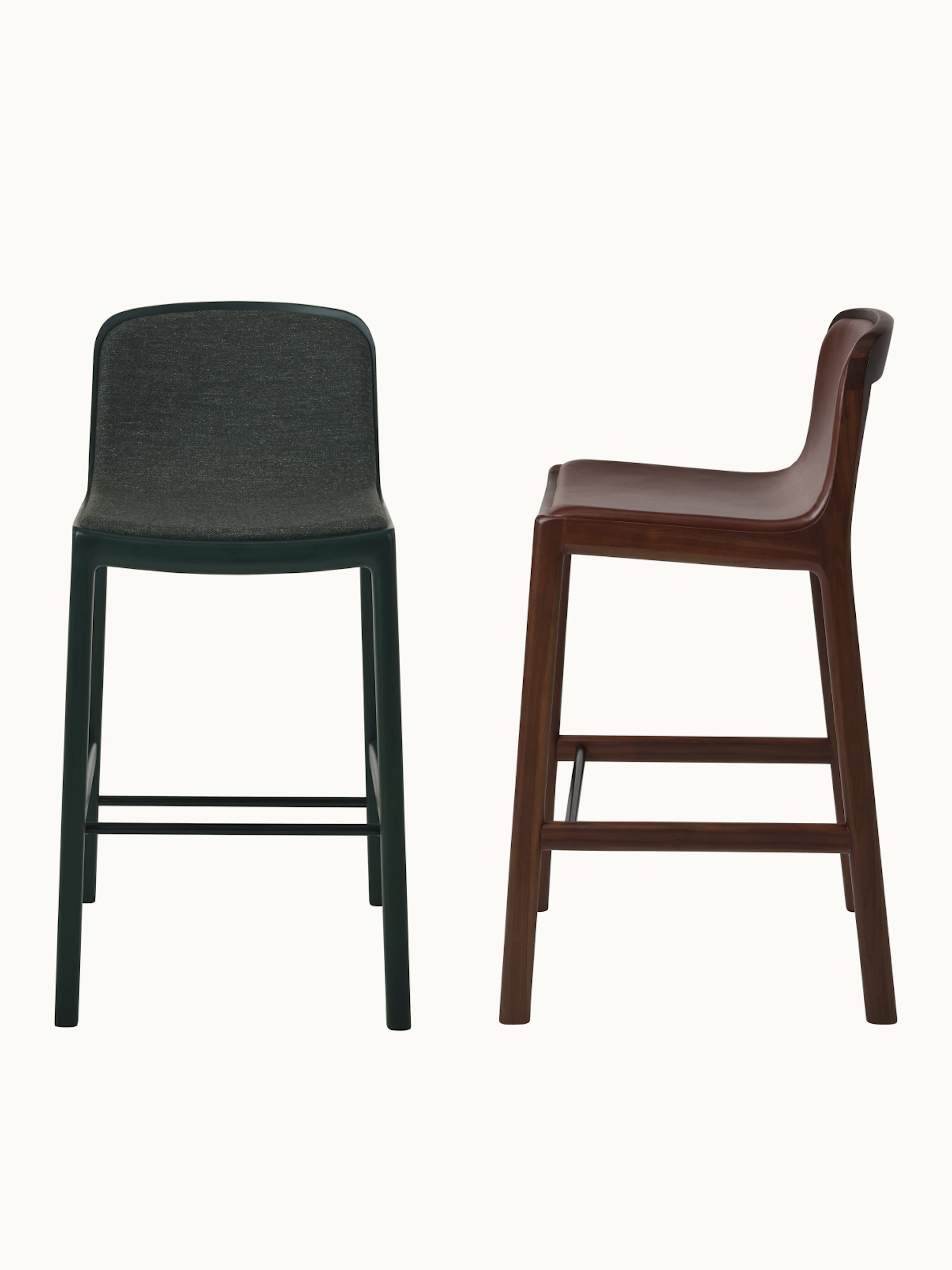 Two fully upholstered Lijn Stools designed by Carole Baijings, one front-facing in Ivy with dark green upholstery, one in Perian Walnut with brown leather upholstery shown at an angle, on a white sweep.