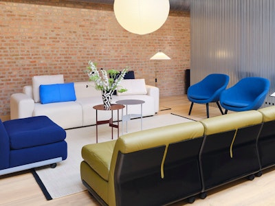 A white sofa, bright blue chairs, and a green sofa from HAY decorate this communal seating area at MillerKnoll Design Days