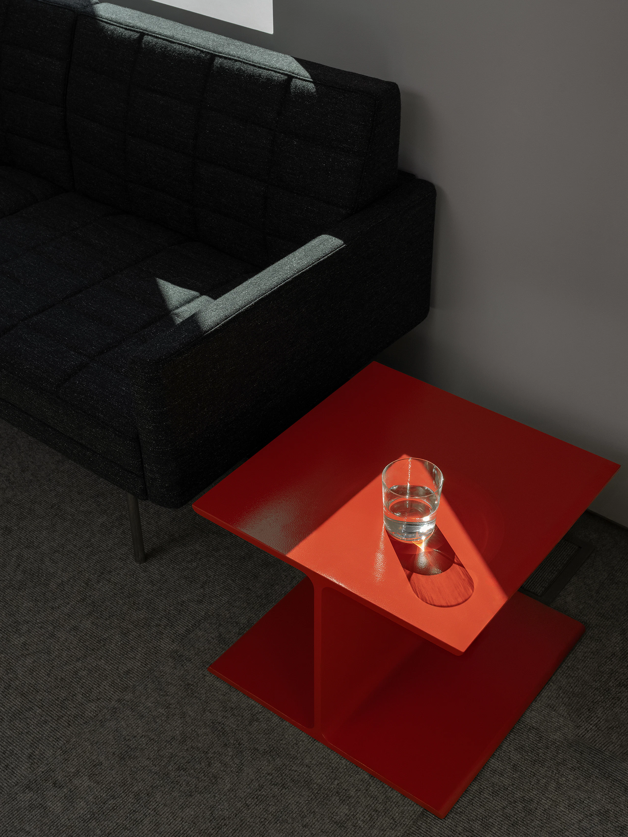 Tuxedo Component Sofa upholstered with Bellano textile in Black Green beside an orange I Beam Side Table in a showroom setting, viewed from above at an angle.