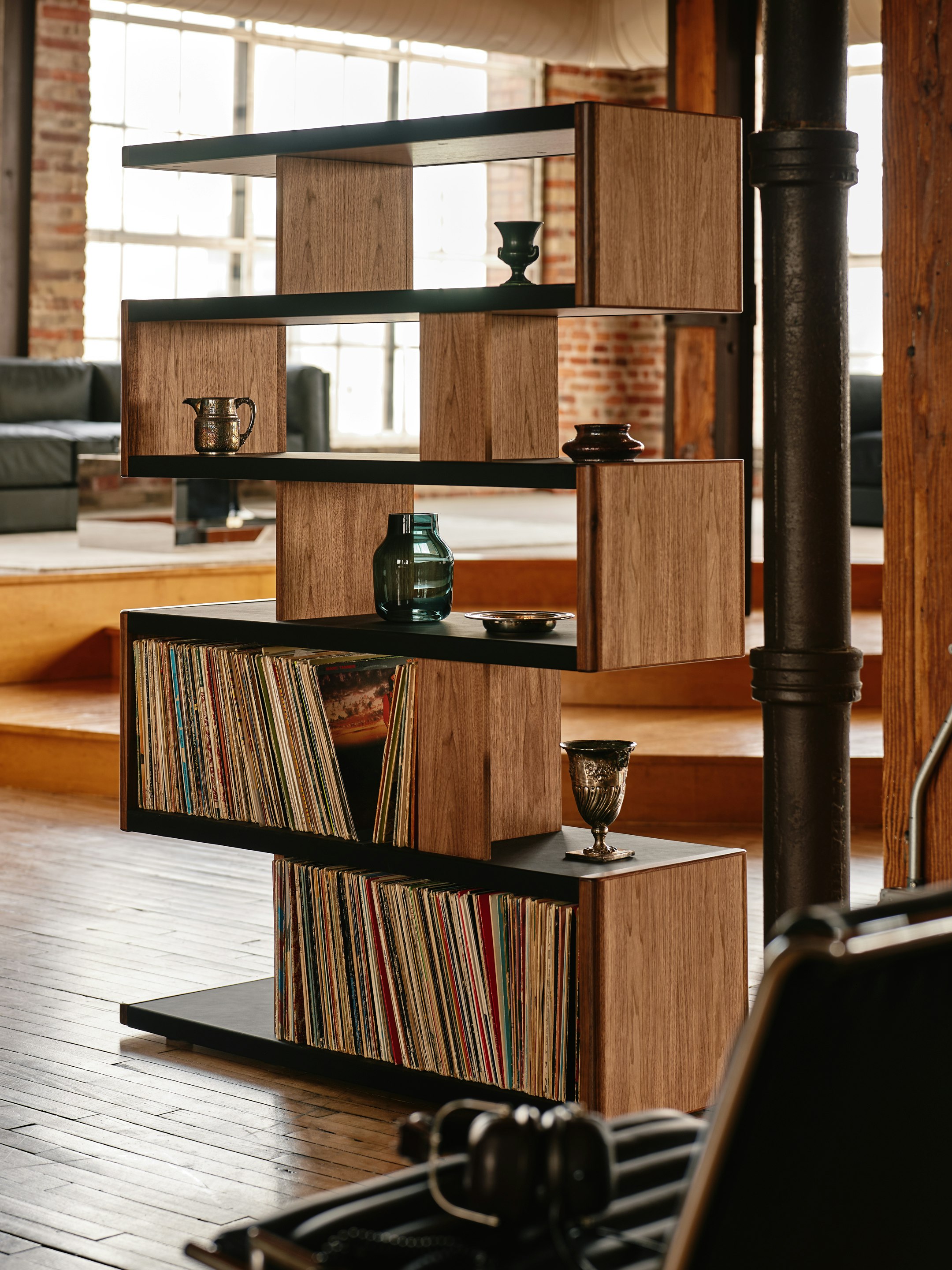 New Canaan High Bookshelf designed by BassamFellows for Geiger in Walnut with Black Leather shown angled in a residential setting with books and objects on shelves.