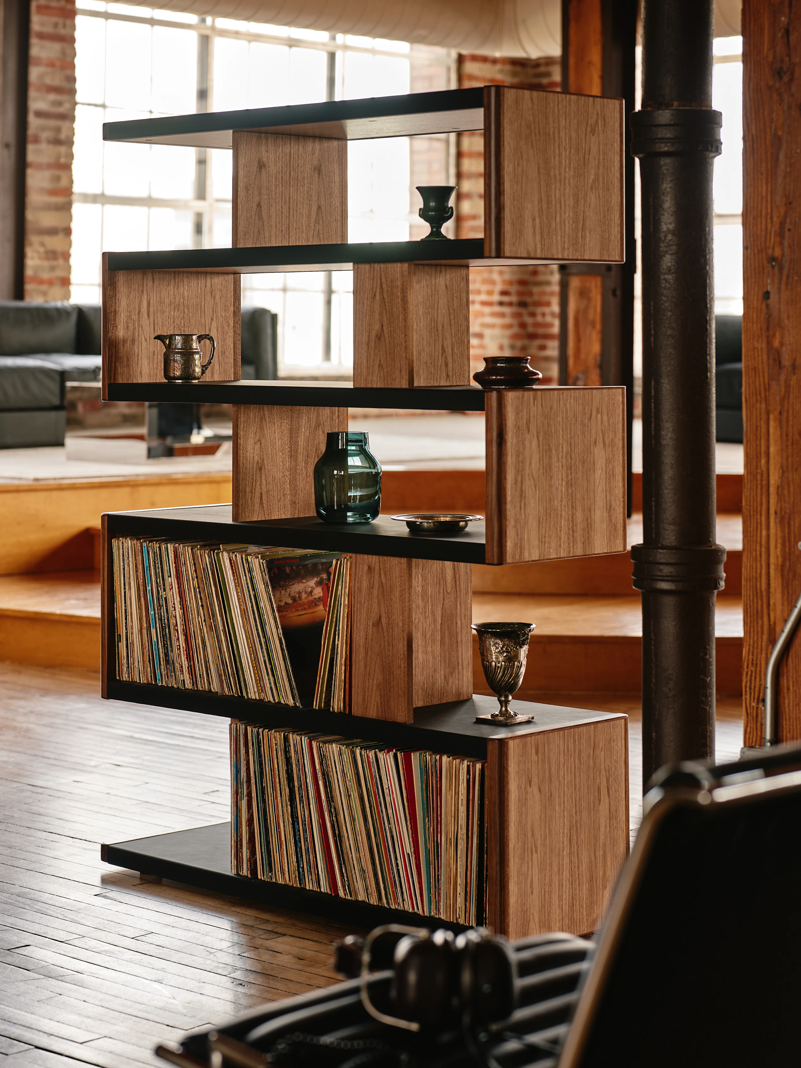 New Canaan High Bookshelf designed by BassamFellows for Geiger in Walnut with Black Leather shown angled in a residential setting with books and objects on shelves.