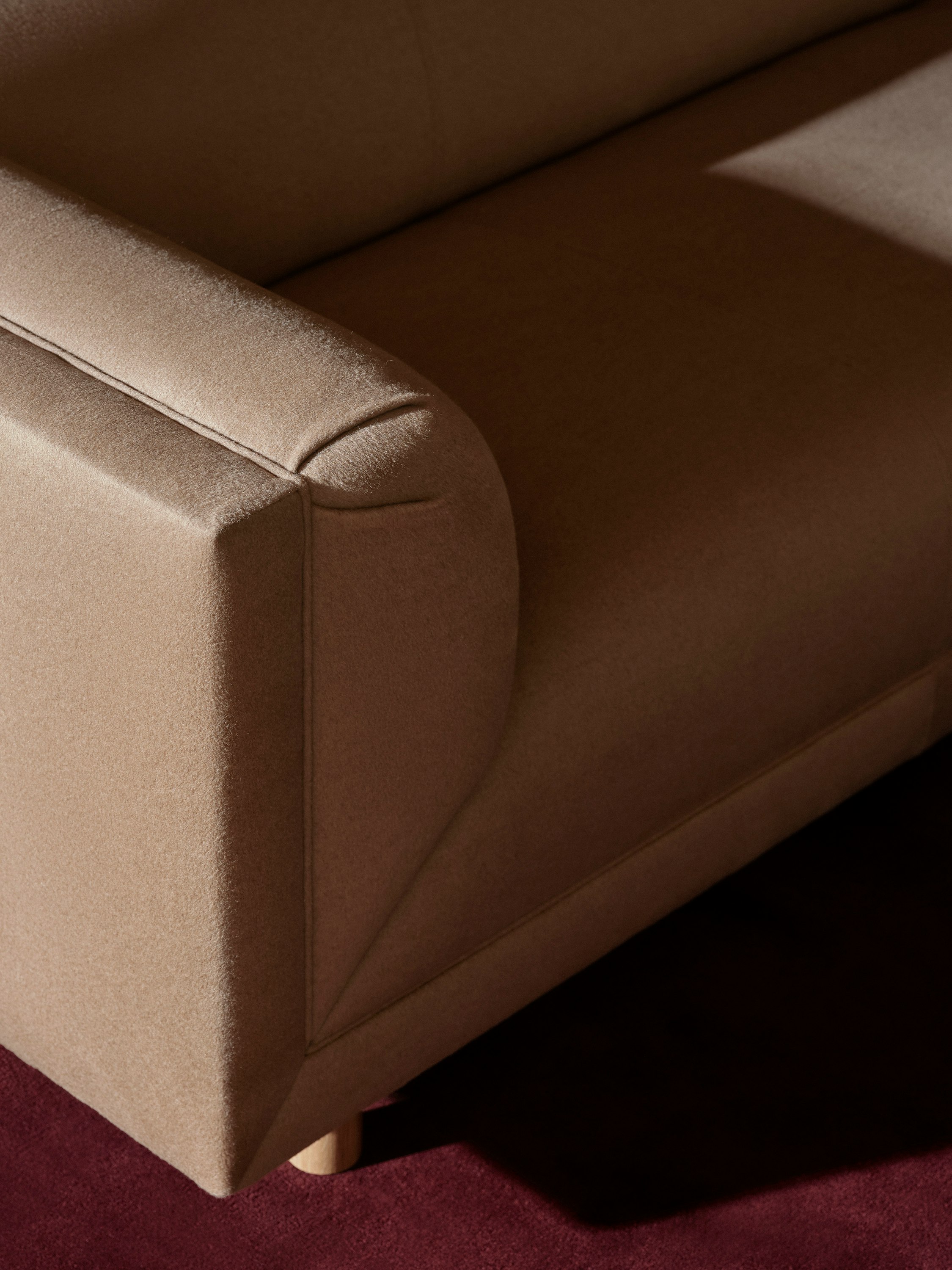 Detail view of a Rolled Arm Sofa designed by Ward Bennett upholstered with Brushed Camel in Natural, viewed from above at an angle on a burgundy rug.