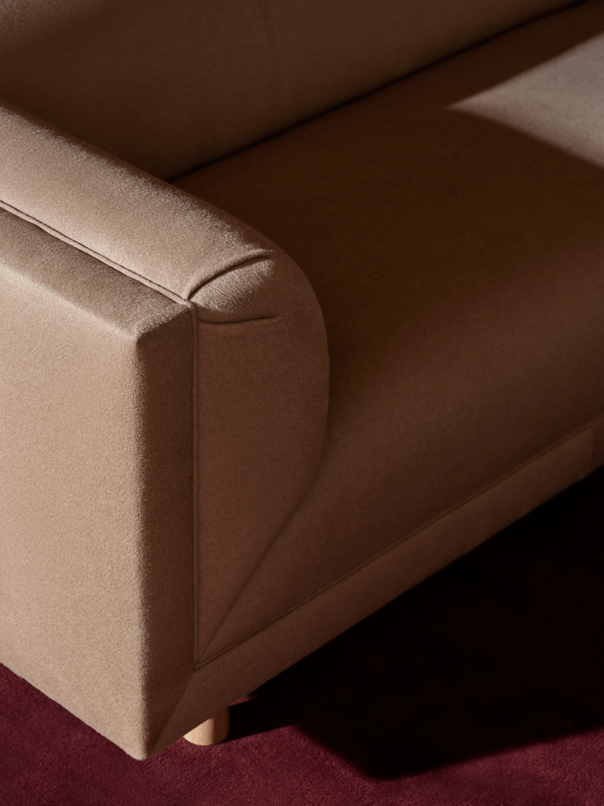 Detail view of a Rolled Arm Sofa designed by Ward Bennett upholstered with Brushed Camel in Natural, viewed from above at an angle on a burgundy rug.