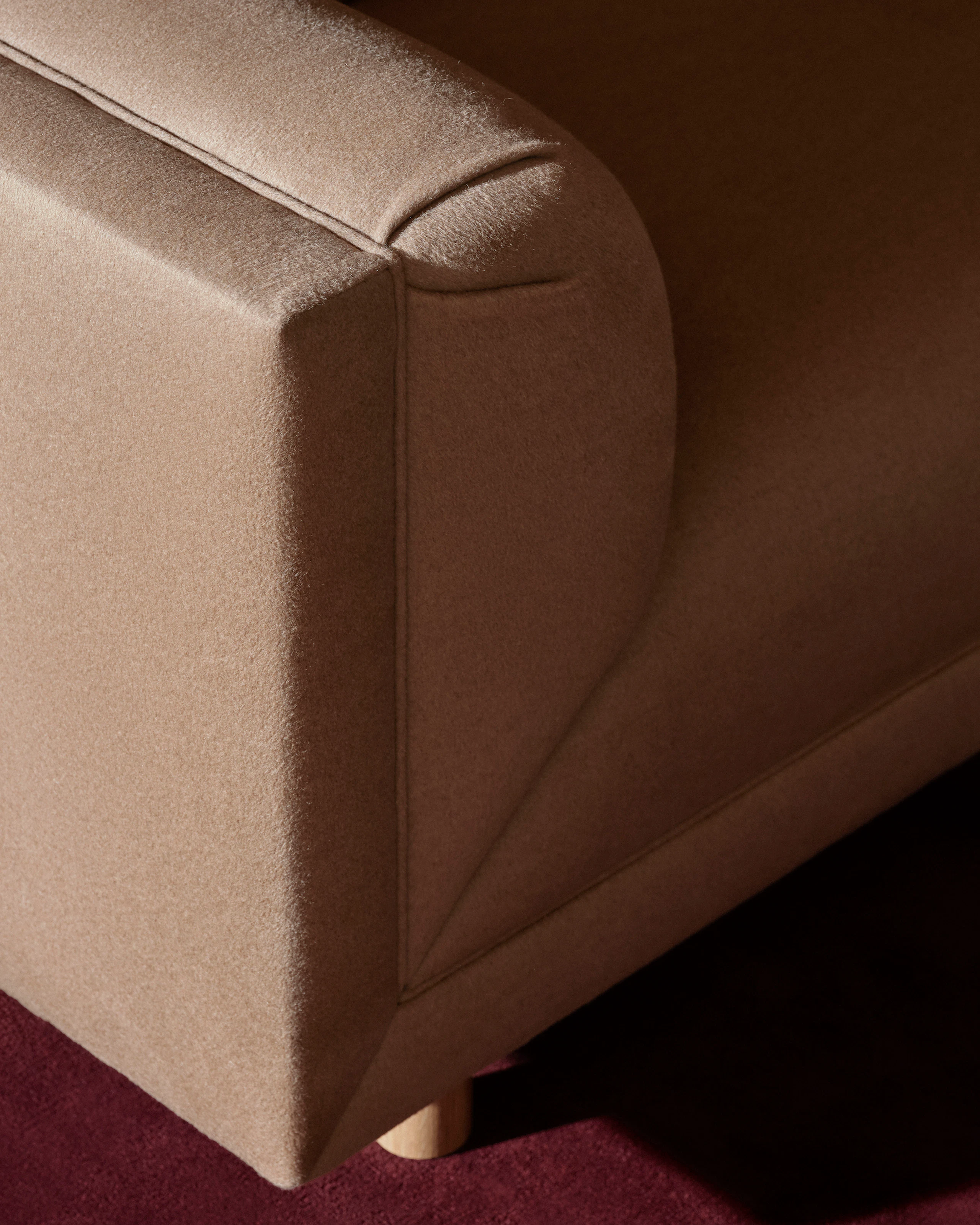 Detail view of a Rolled Arm Sofa designed by Ward Bennett upholstered with Brushed Camel in Natural, viewed from above at an angle on a burgundy rug.