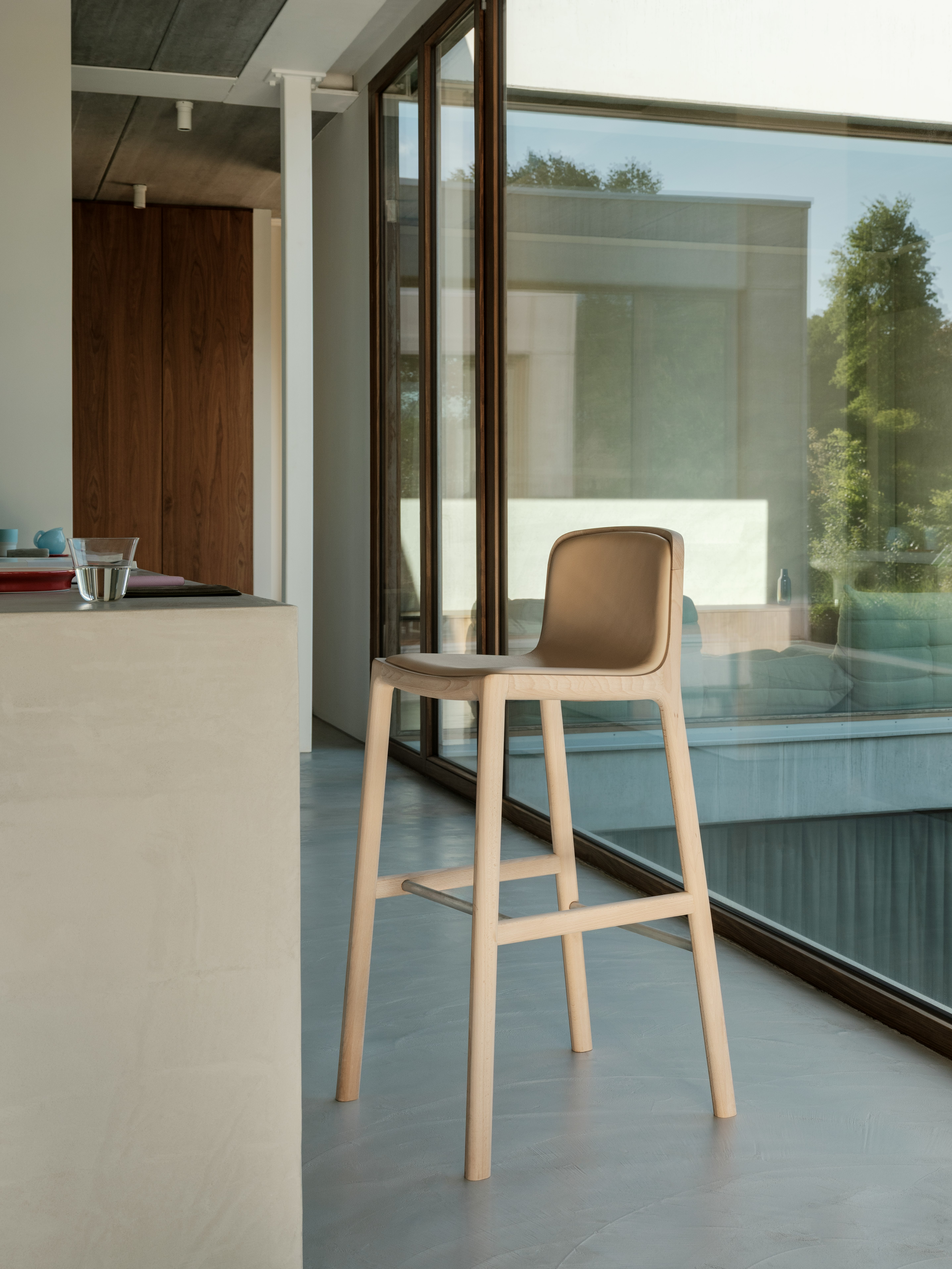 Lijn Stool designed by Carole Baijings for Geiger with leather upholstered seat and back on a matte wood frame viewed at an angle in a styled environment.