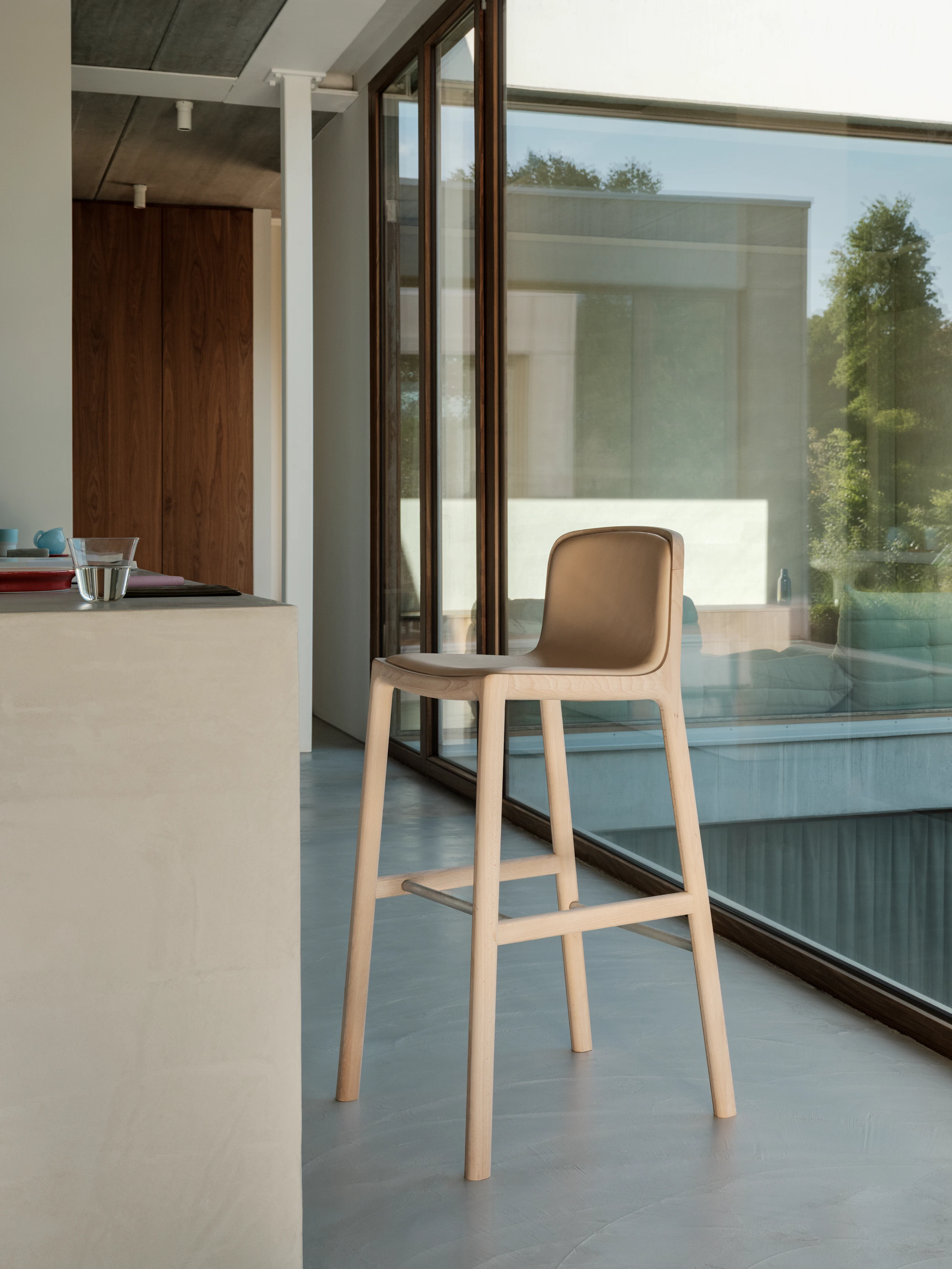 Lijn Stool designed by Carole Baijings for Geiger with leather upholstered seat and back on a matte wood frame viewed at an angle in a styled environment.