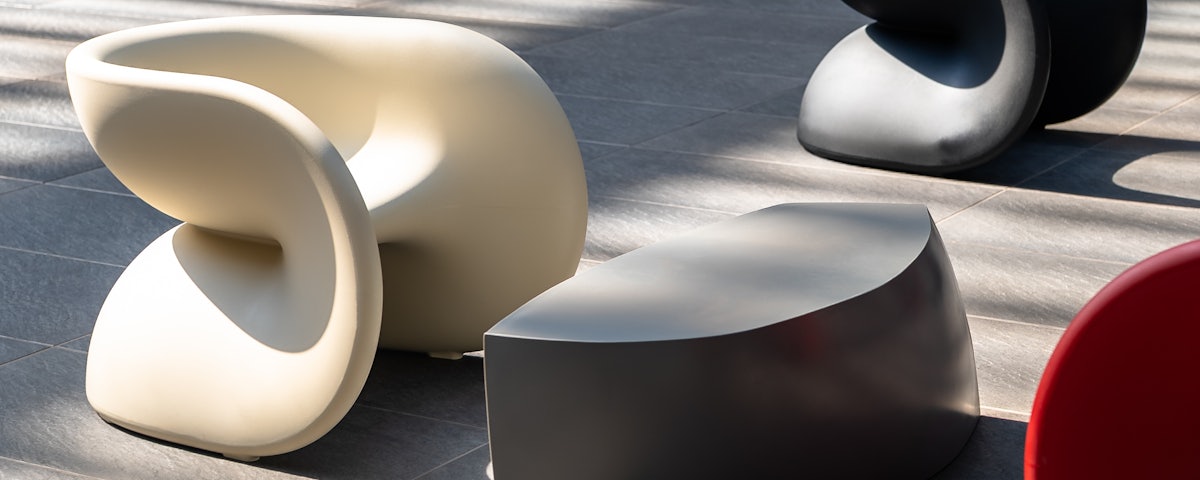 A white Fortune Chair in front of an outdoor coffee table in a stone patio setting