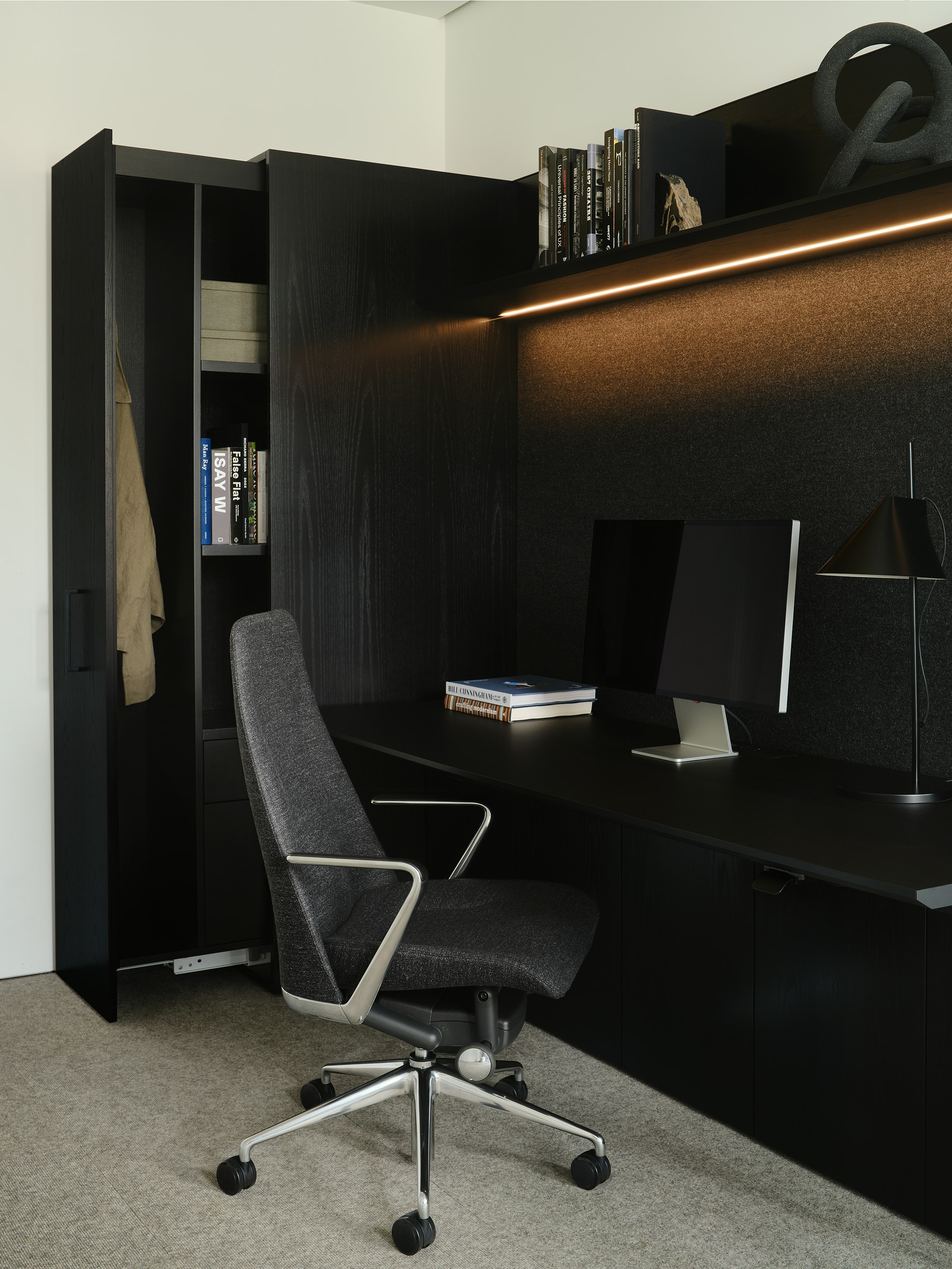 Geiger One Casegoods in Ebonized Flat Cut Ash veneer shown at an angle with an open wardrobe, overhead shelf with integrated lighting, and Taper chair.