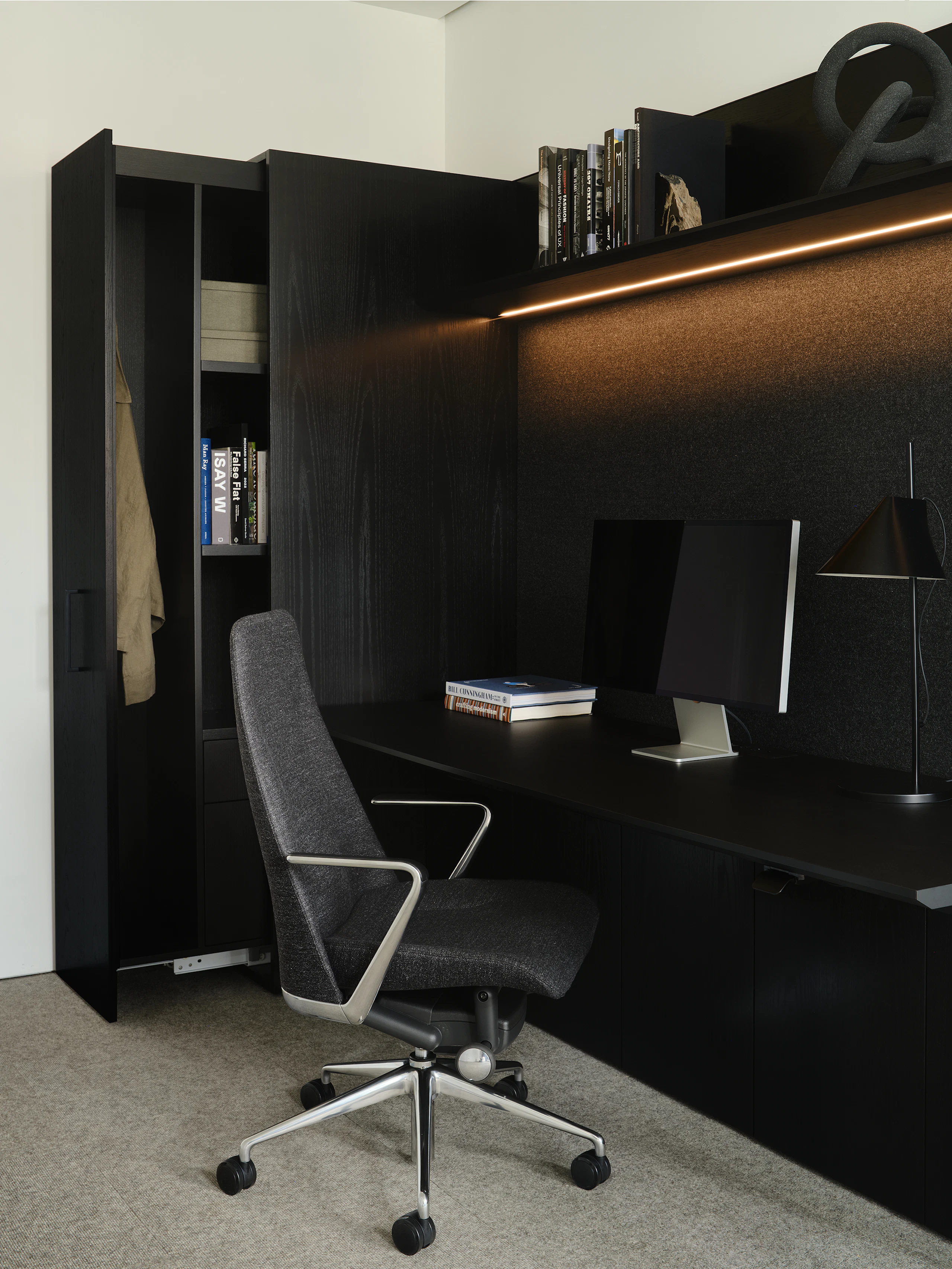 Geiger One Casegoods in Ebonized Flat Cut Ash veneer shown at an angle with an open wardrobe, overhead shelf with integrated lighting, and Taper chair.