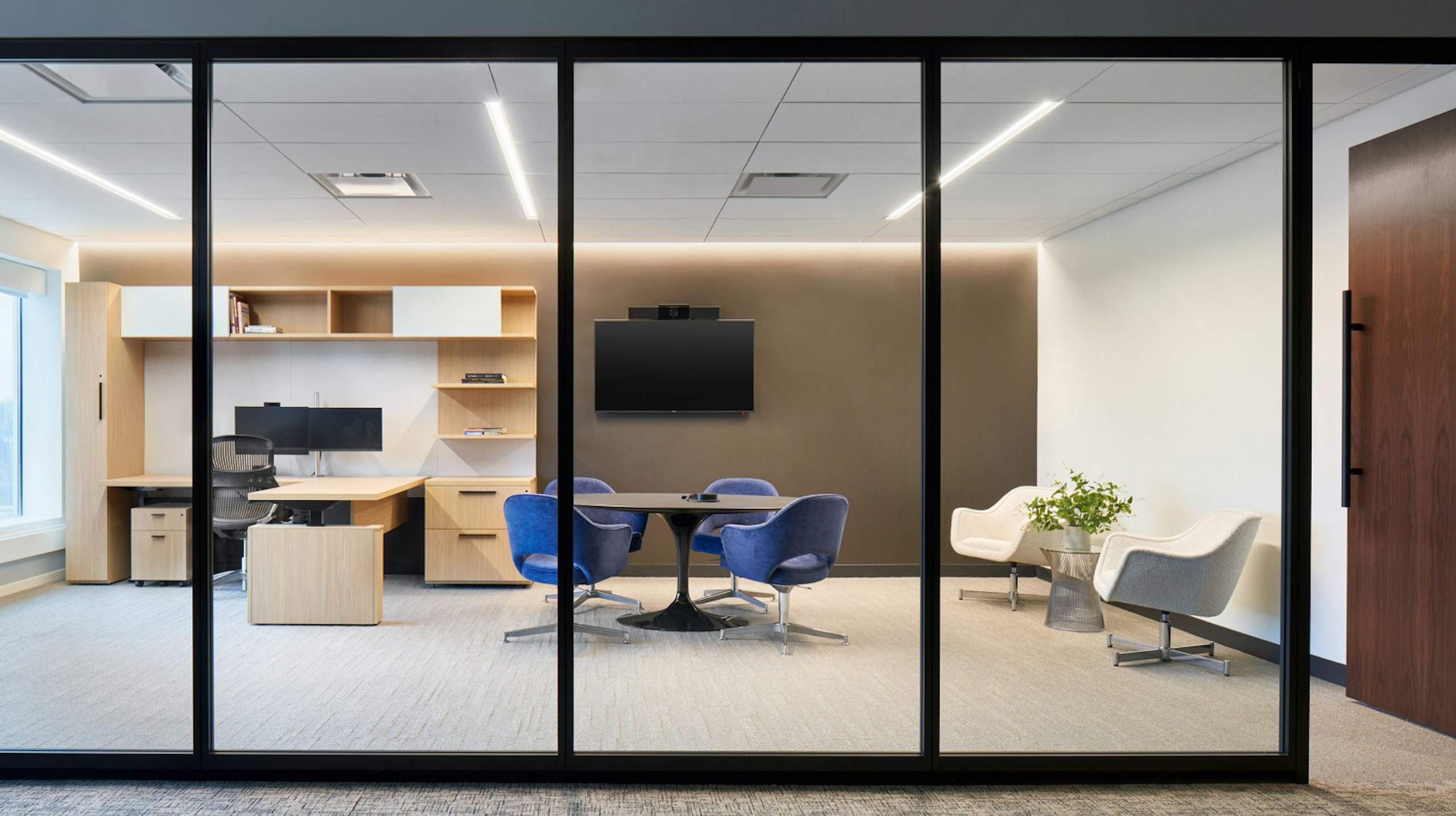 Four blue Knoll Saarinen Executive armchairs surrounding a round table, two Saarinen white executive armchairs off to the side, and a desk system in a large private office