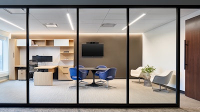 Four blue Knoll Saarinen Executive armchairs surrounding a round table, two Saarinen white executive armchairs off to the side, and a desk system in a large private office