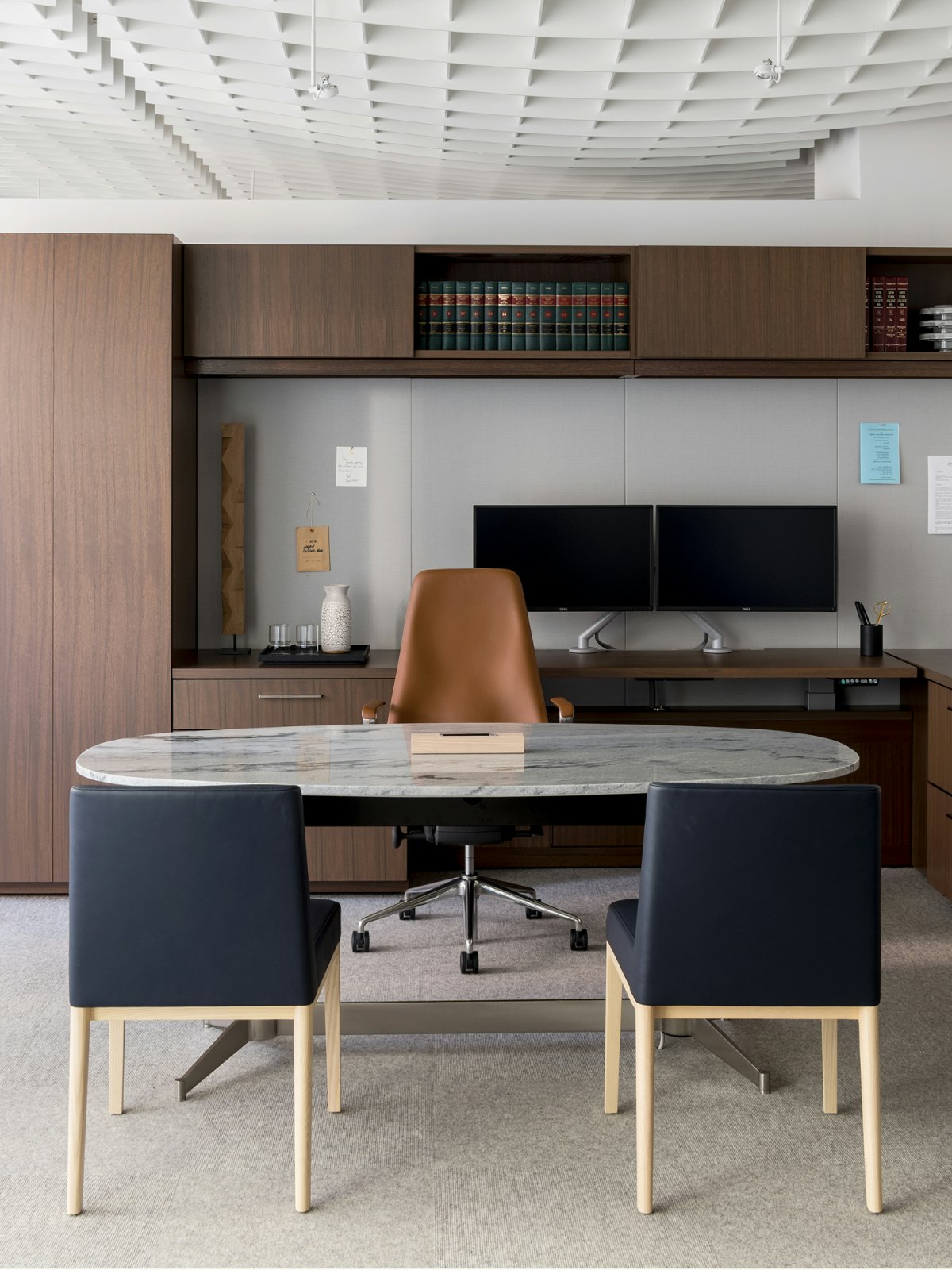 A private office with an oval table with a stone top; a leather Taper Chair; and two blue Nessel Side Chairs.