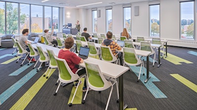 Students sitting in rows of green and white chairs while a teacher leads a class