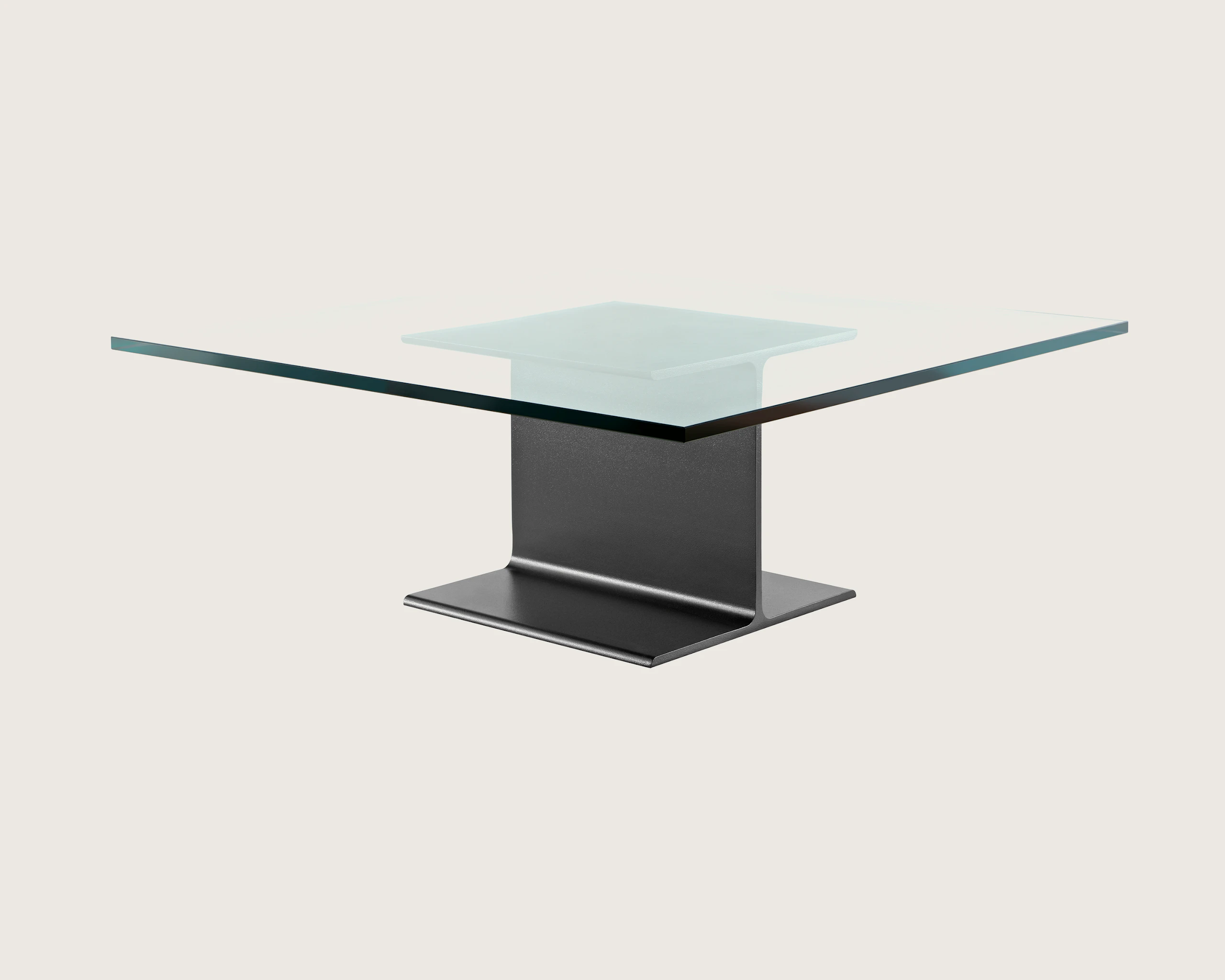 Partial angled view of a square I Beam coffee table with a glass top and black cast-aluminum pedestal.