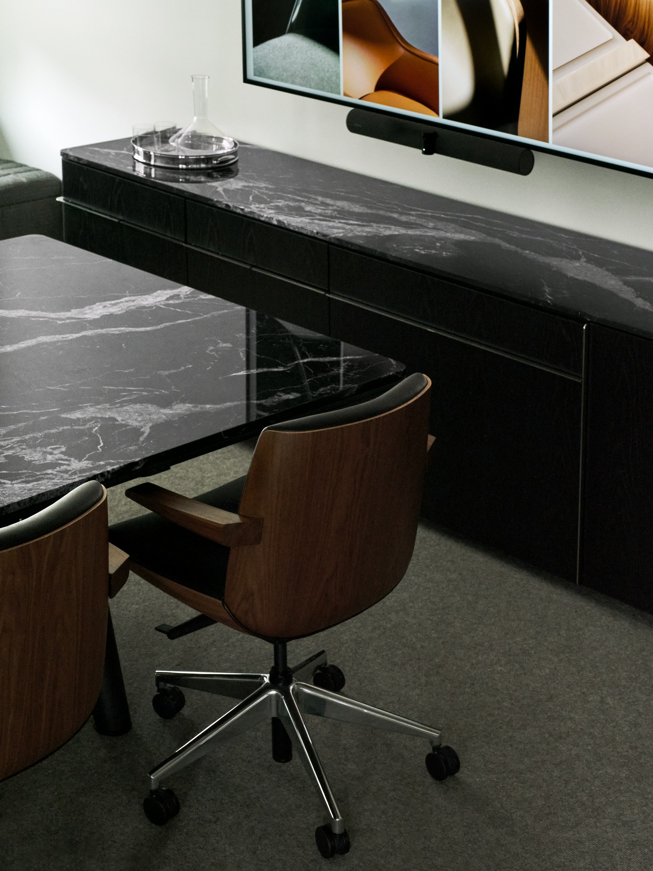 Two low back Clamshell Conference Chairs in Walnut upholstered with black lather beside an Ascent Conference Table and Credenza, both with Nero Marquina Marble tops, viewed from behind at an angle.