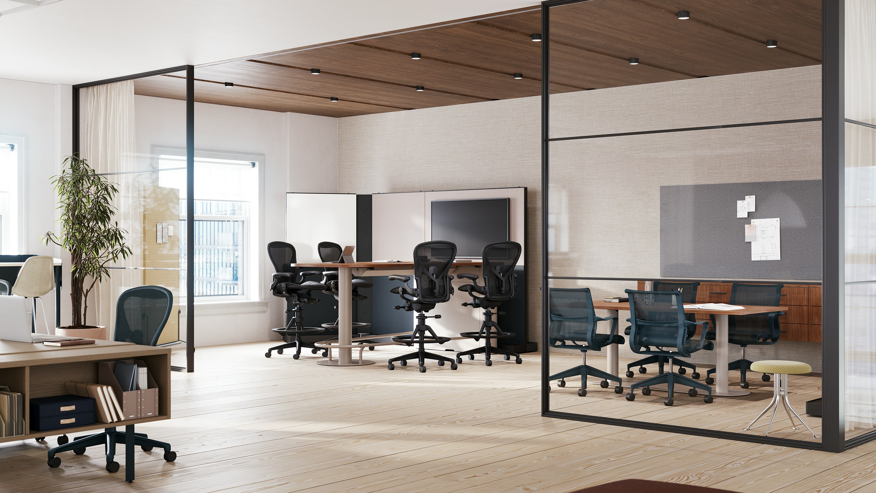 A collaborative space featuring four Aeron stools in dark gray around a table and monitor and four Setu chairs around a meeting table.