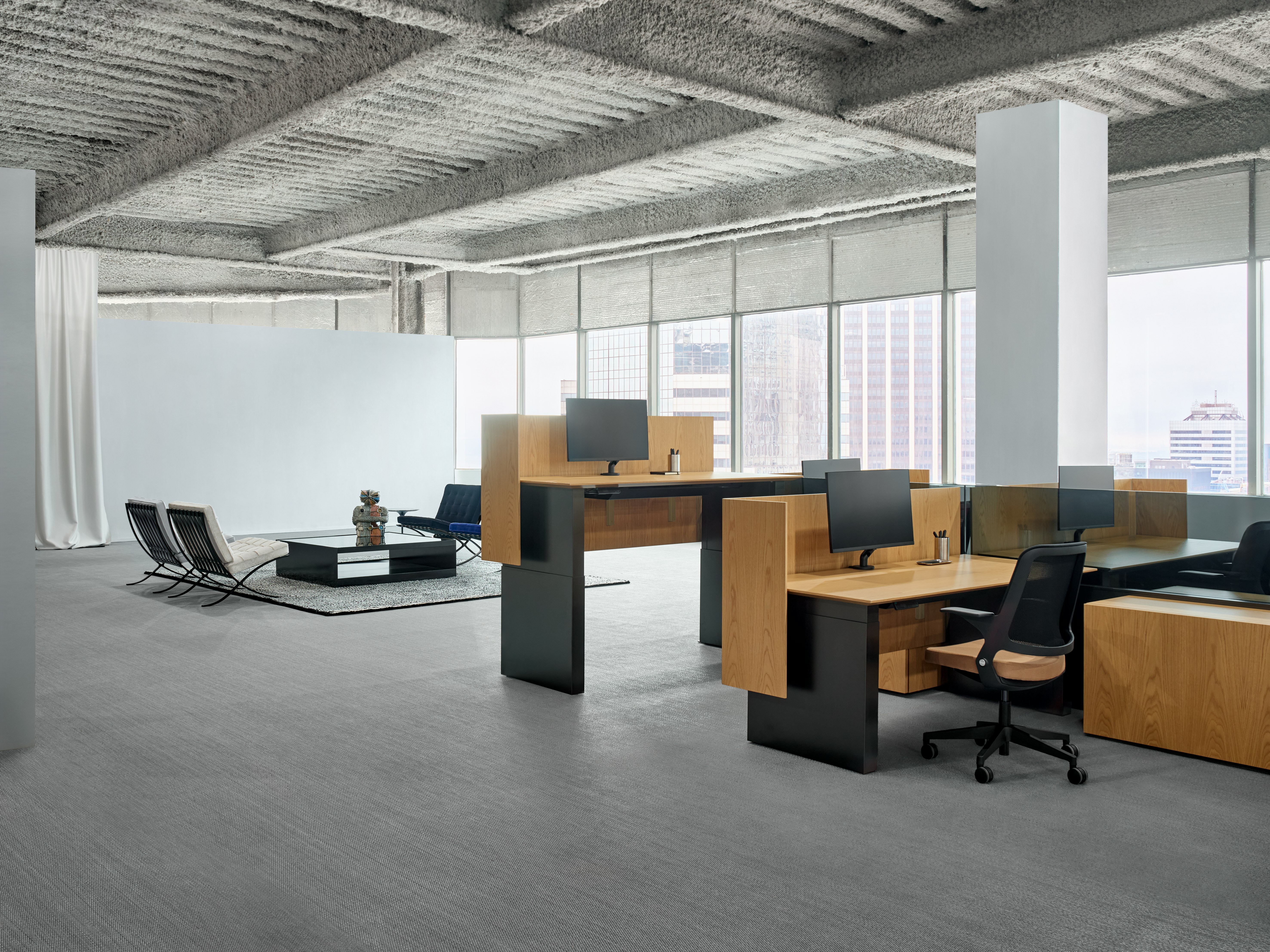 A group of workstations with height adjustable work tables are in front of a lounge area with four chairs.