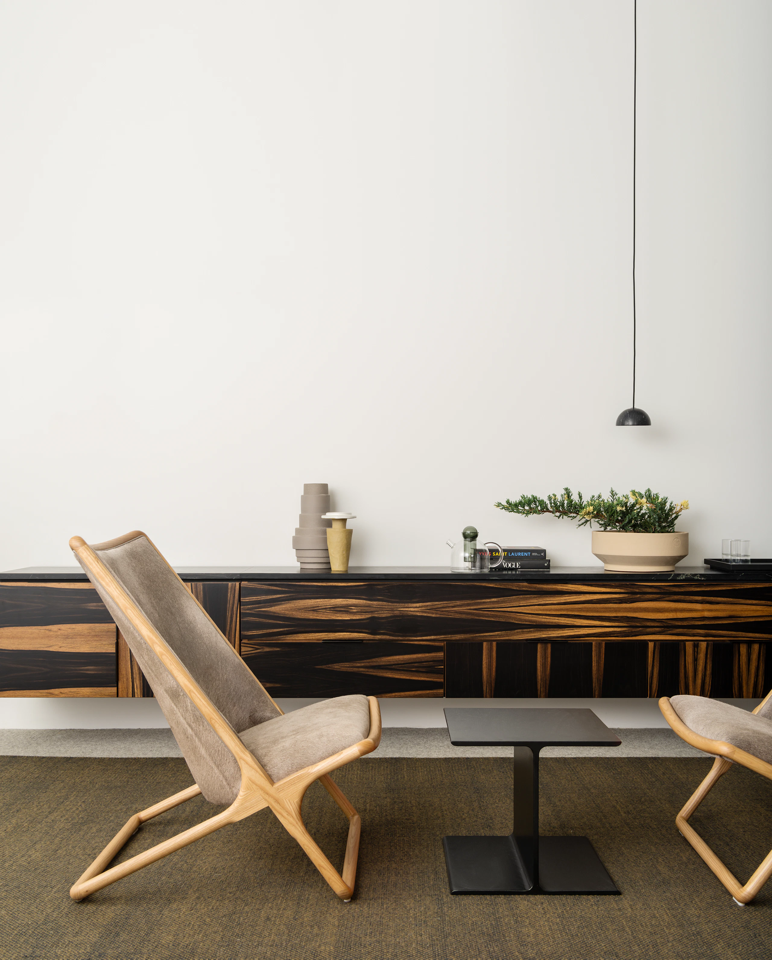 A small interaction space featuring two wood-frame Scissor Chairs in Maharam tuft thunder textile on either side of a black I Beam side table.