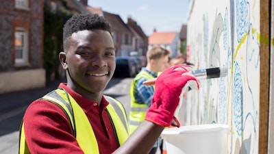 A person wearing a yellow hi-vis jacket and red gloves painting a mural on a wall.