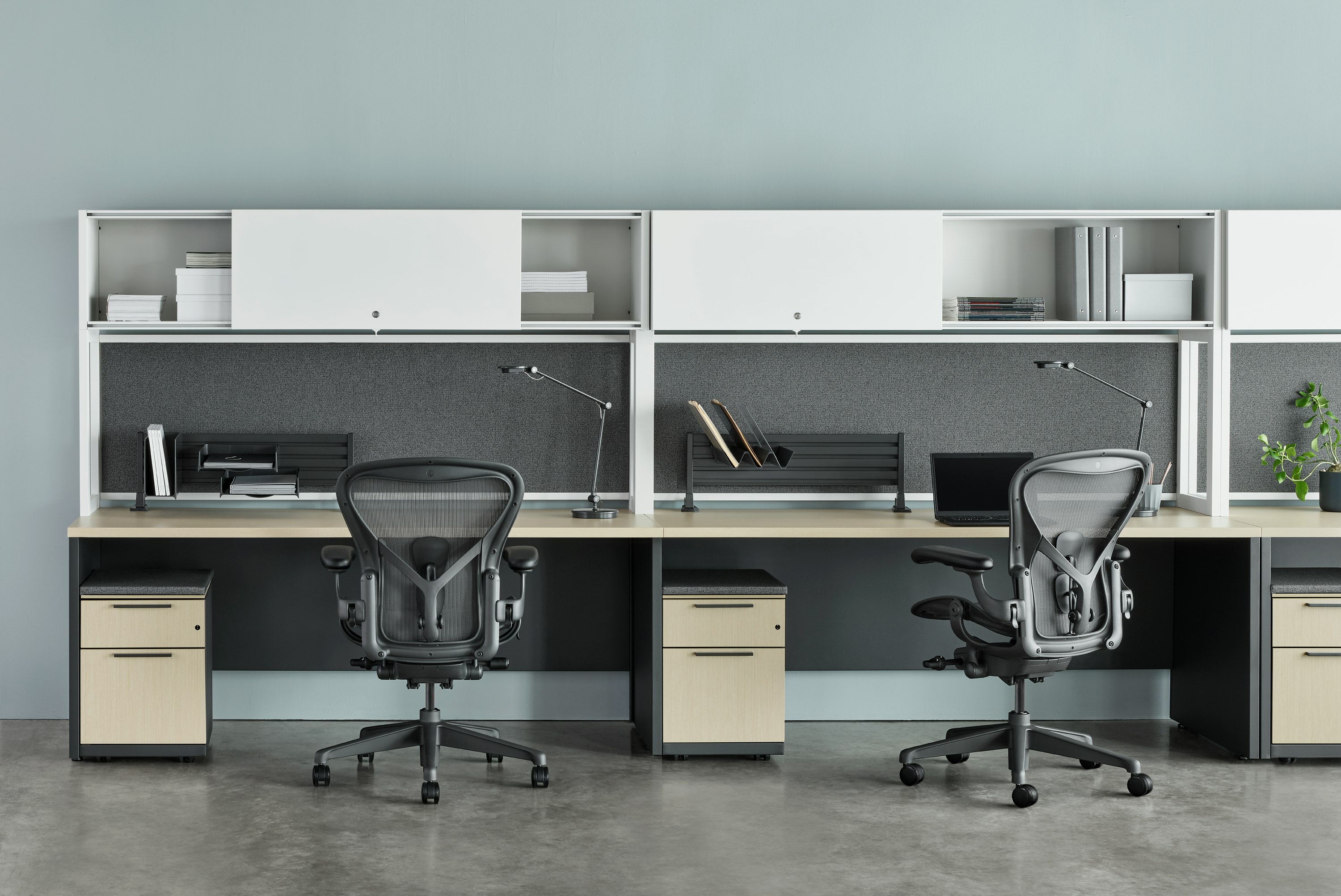 Two Canvas Metal Desks with white upper storage, grey tackboards, and grey Aeron Chairs.