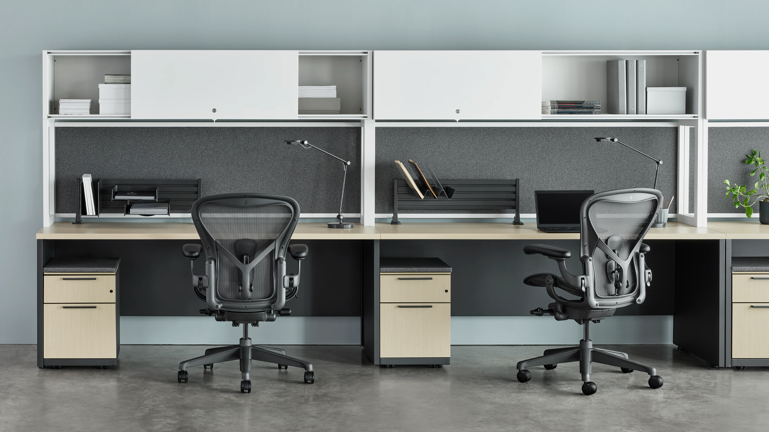 Two Canvas Metal Desks with white upper storage, grey tackboards, and grey Aeron Chairs.
